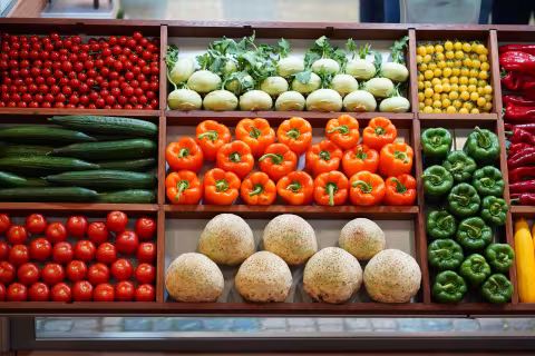 Eine Gemüseauslage mit verschiedenen Sorten. Darunter rote und gelbe Kirschtomaten, orangene und grüne Paprika sowie Salatgurken