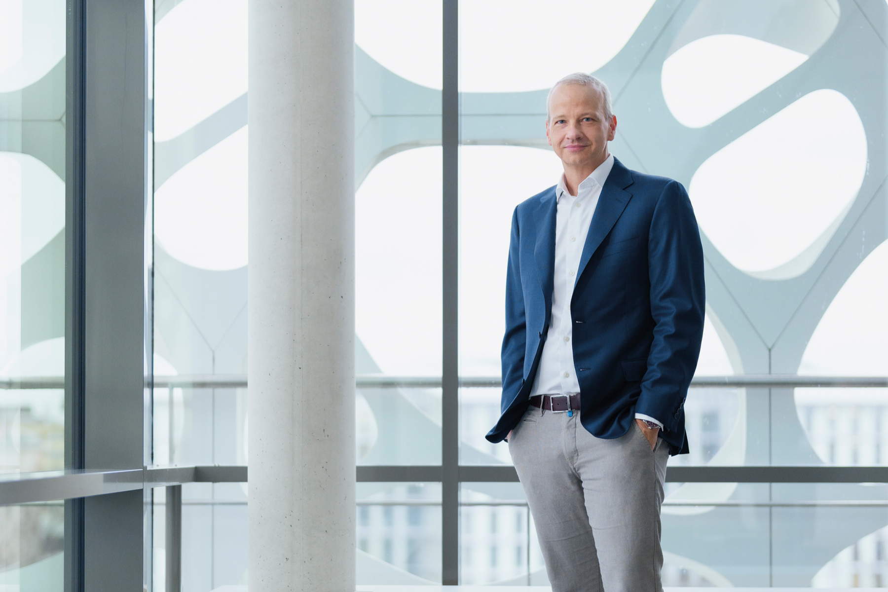 Markus Kamieth, Vorstandsvorsitzender von BASF, steht in einem modernen Gebäude mit großen Fenstern, trägt einen dunkelblauen Blazer, weißes Hemd und graue Hose