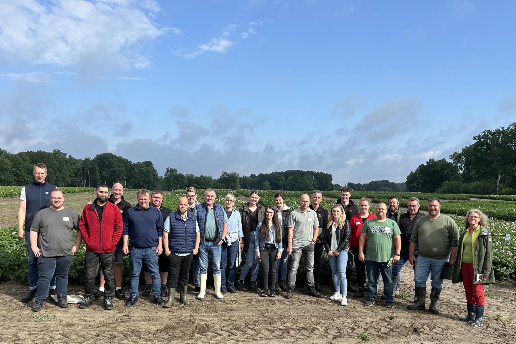 Kleingruppe steht auf Acker vor Kartoffelpflanzen unter blauem Himmel
