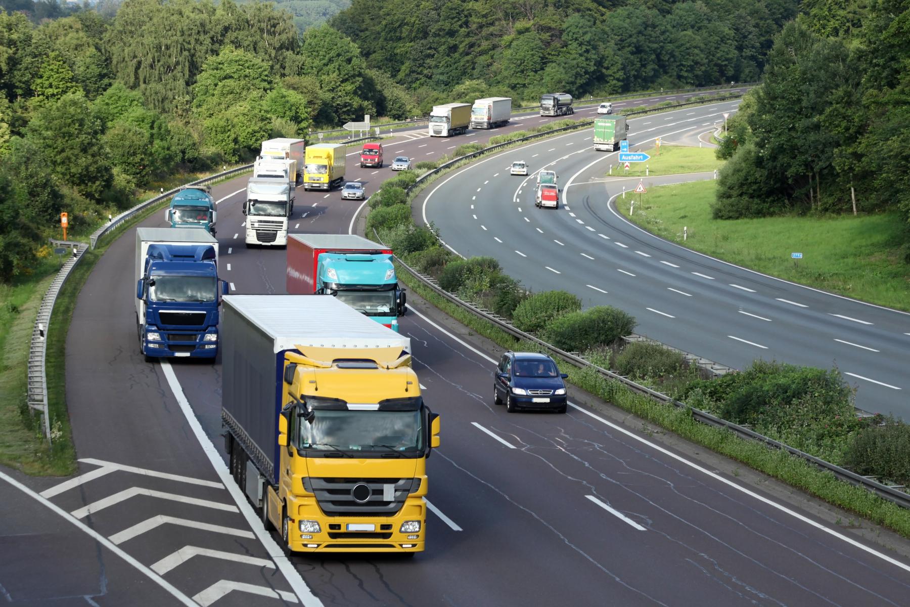 Mehrere Lastwagen und Autos fahren auf einer mehrspurigen Autobahn in einer grünen, bewaldeten Landschaft