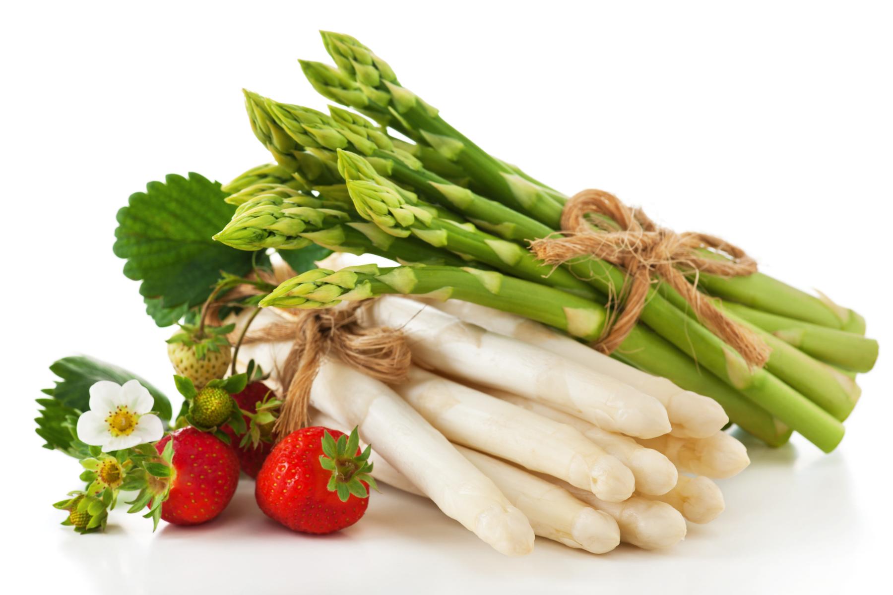 ündel grüner und weißer Spargel zusammengebunden mit Juteband, daneben frische Erdbeeren und Erdbeerblüten