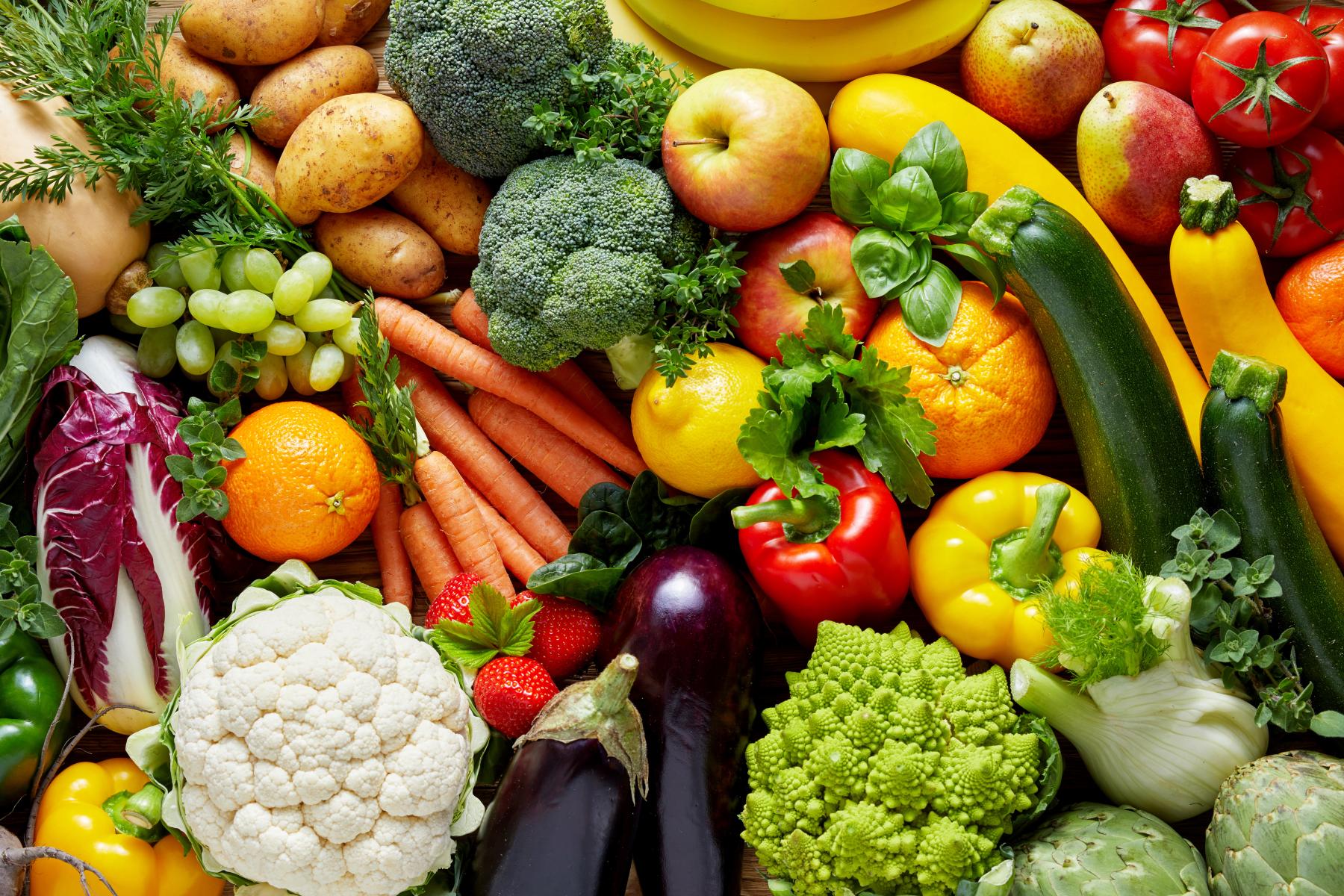 Verschiedene frische Gemüsesorten und Früchte, darunter Karotten, Paprika, Brokkoli, Tomaten, Auberginen, Blumenkohl, Zucchini, Trauben und Orangen