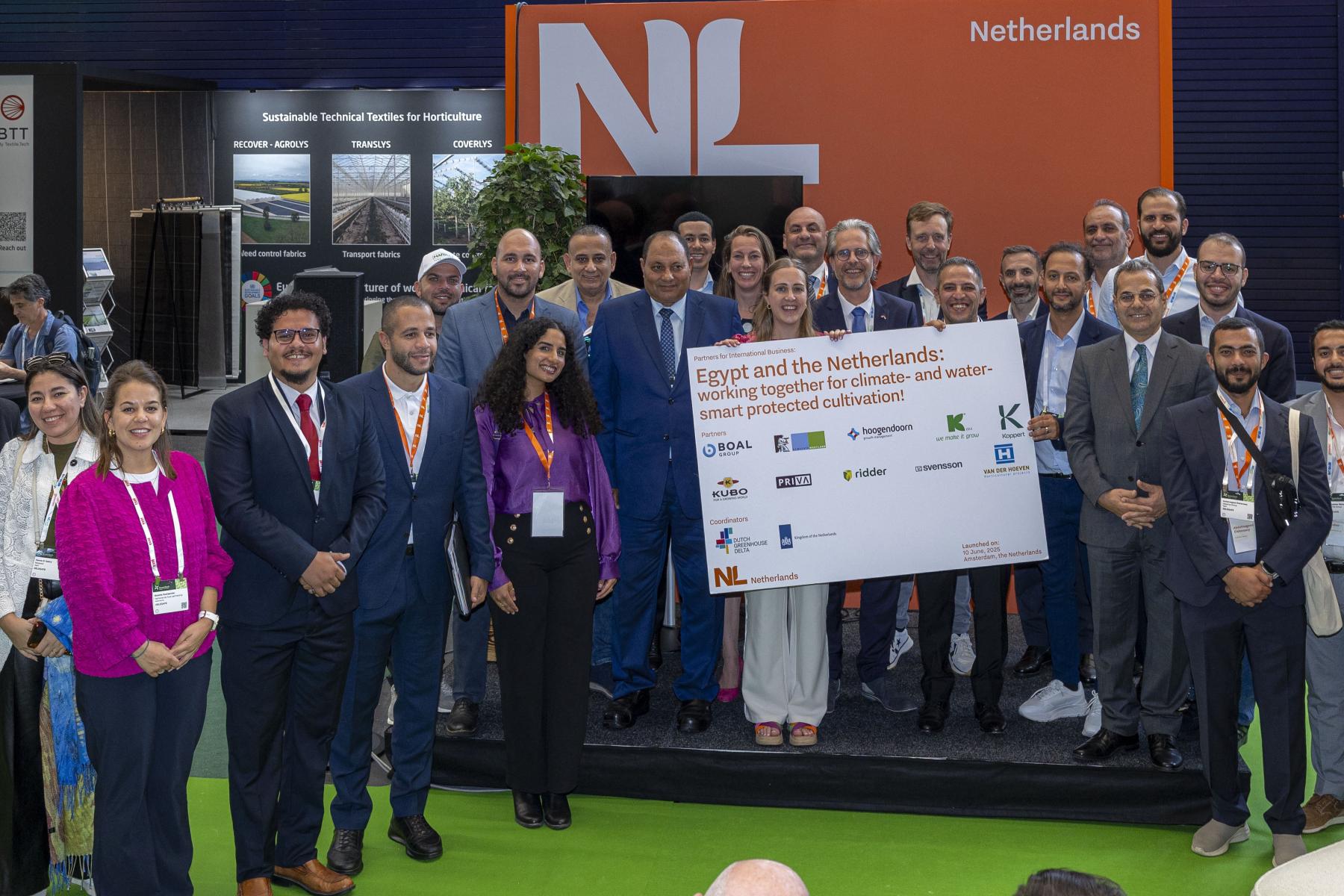 Gruppe von Personen auf einer Messe vor einem orangefarbenen Stand mit dem Schriftzug 'Netherlands', halten ein großes Schild mit dem Titel 'Egypt and the Netherlands: working together for climate- and water-smart protected cultivation'
