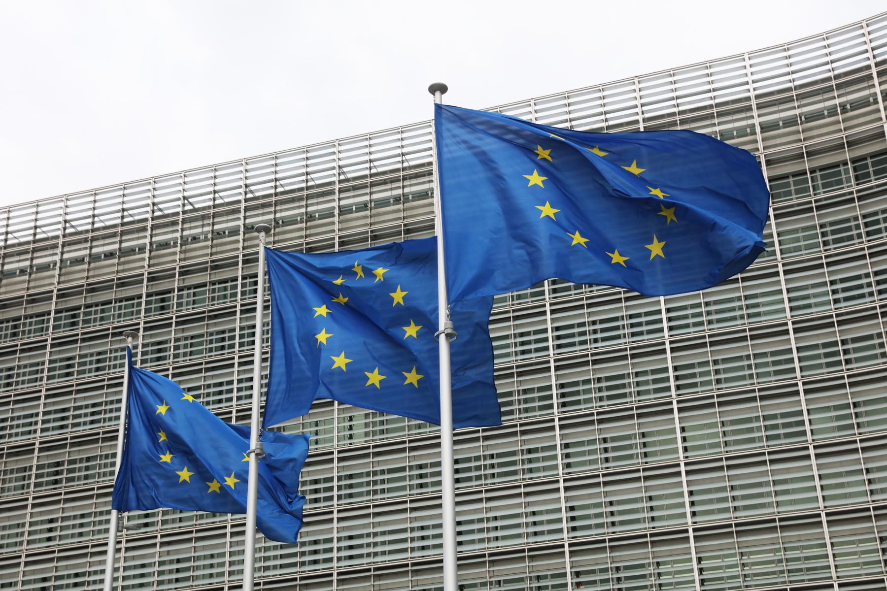 Drei wehende Europaflaggen vor einem modernen Glasgebäude