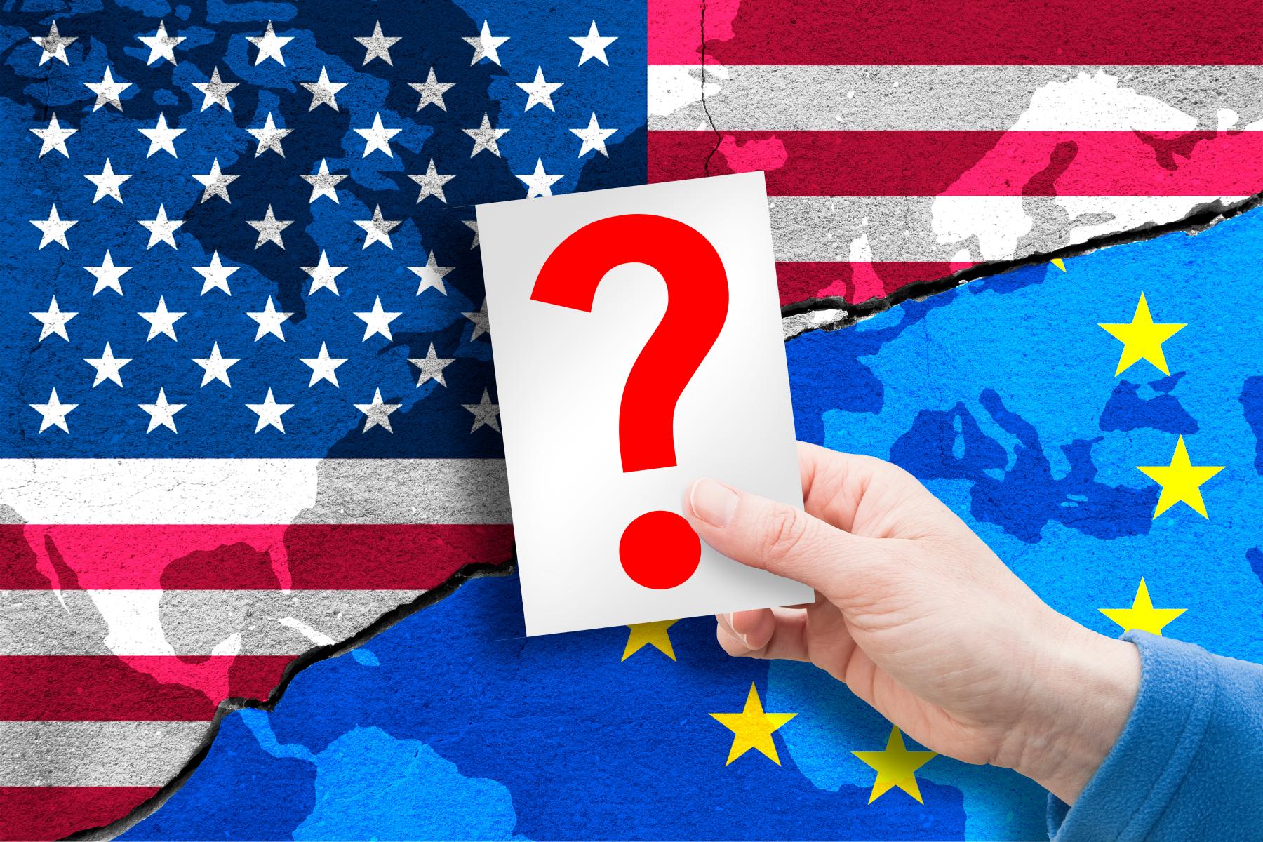 Hand hält Karte mit rotem Fragezeichen vor zerrissener US-Flagge und EU-Flagge, symbolisiert Ungewissheit in Beziehungen