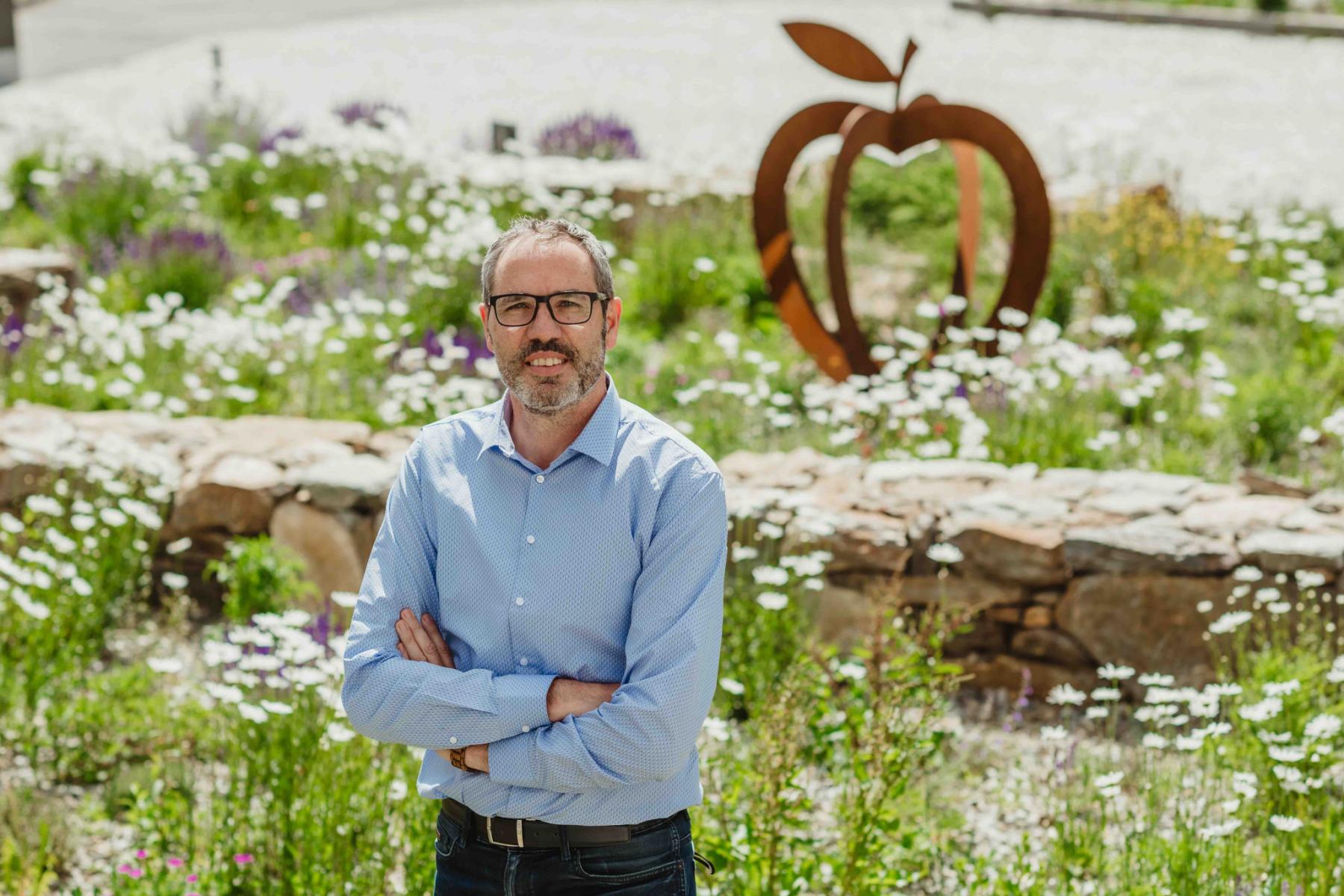 Gerhard Eberhöfer stehend mit verschränkten Armen, im Hintergrund Gräser und Wildblumen