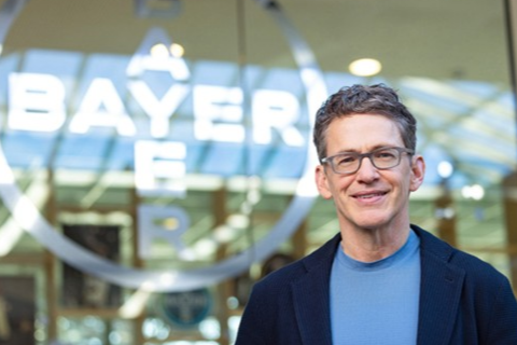 Bill Anderson steht vor dem Bayer-Logo in einem modernen Gebäude