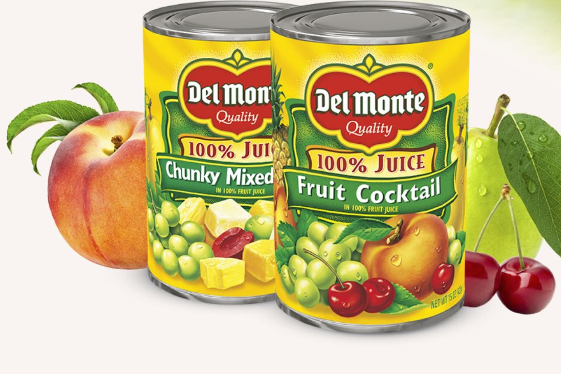Zwei Del Monte Dosen mit Fruchtcocktail und Chunky Mixed Frucht in 100% Fruchtsaft, umgeben von Pfirsich, Trauben und Kirschen