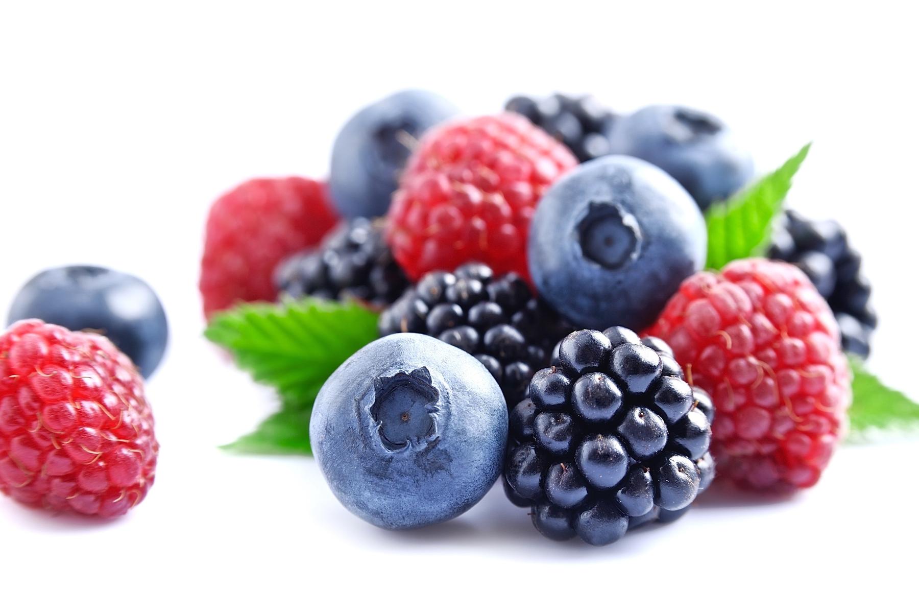 Verschiedene Beeren wie Himbeeren, Heidelbeeren und Brombeeren mit grünen Blättern auf weißem Hintergrund