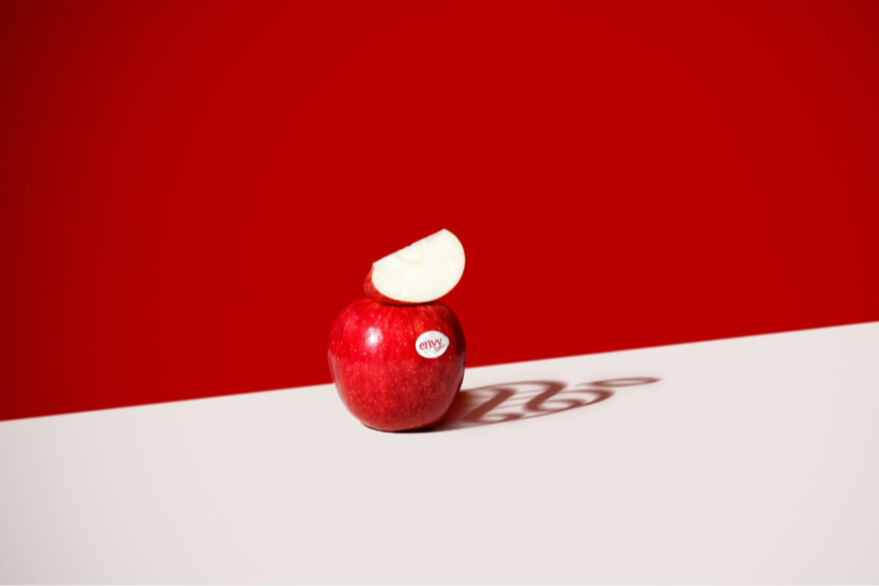 Roter Envy-Apfel mit Aufkleber, auf dem ein Apfelstück aufliegt, roter Hintergrund