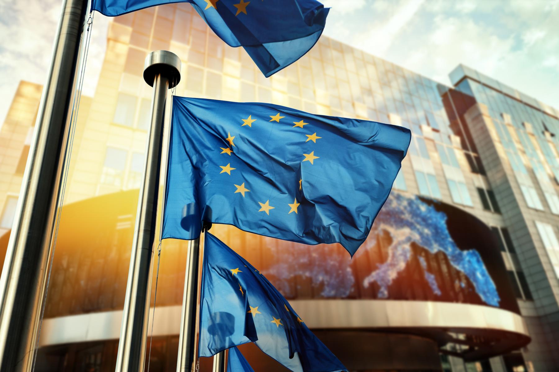 Mehrere wehende Europaflaggen vor einem modernen Gebäude mit Glasfassade
