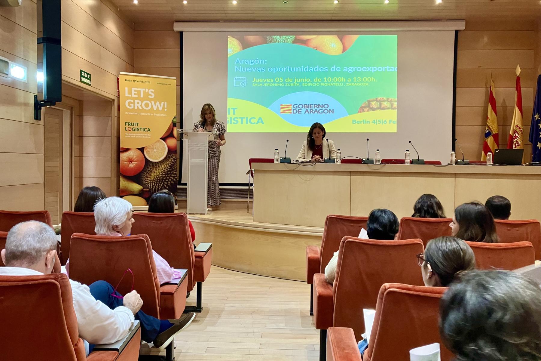 Amparo Cuéllar Hernandis spricht am Rednerpult, Silvia de Juanes sitzt am Tisch, Veranstaltung zur Förderung von Agrarexporten in Aragonien, Publikum im Saal