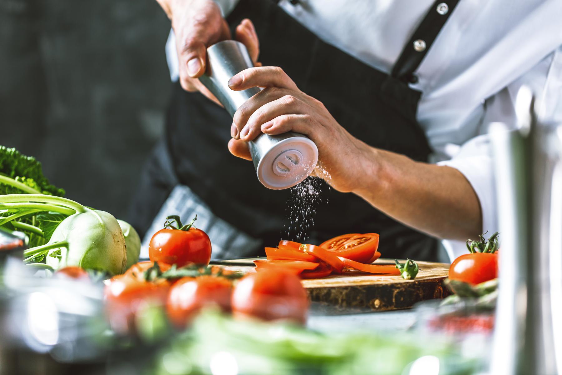 Koch streut Salz über Tomaten