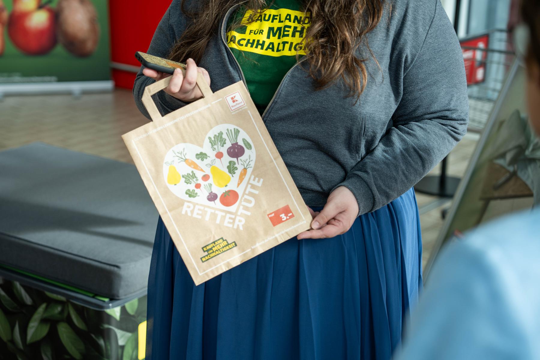 Frau hält eine Papiertüte mit Herzmotiv und der Aufschrift 'Rettertüte' und '3 €' in der Hand