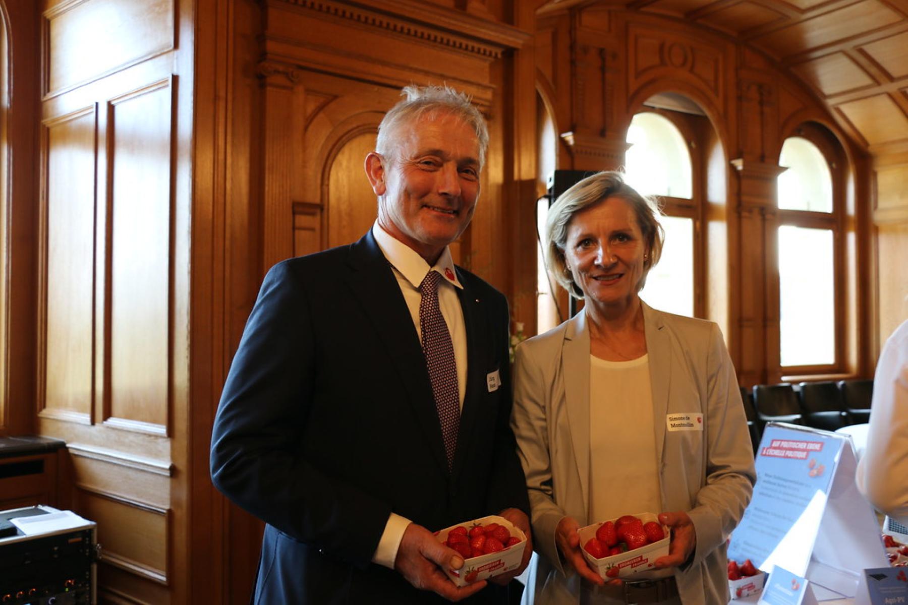 Simone de Montmollin und Jürg Hess stehen nebeneinander und halten jeweils eine Schale mit Erdbeeren