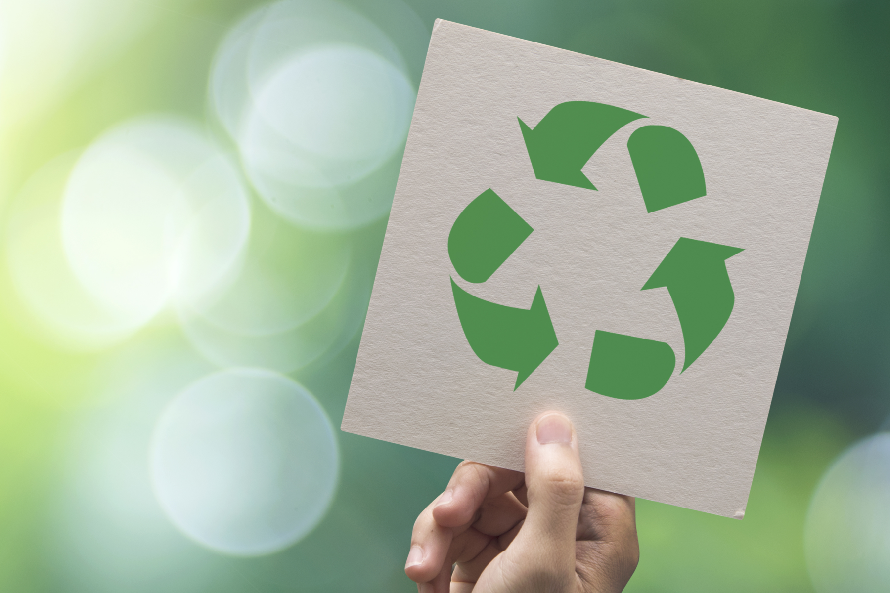 Hand hält Karte mit grünem Recycling-Symbol vor unscharf grünem Hintergrund