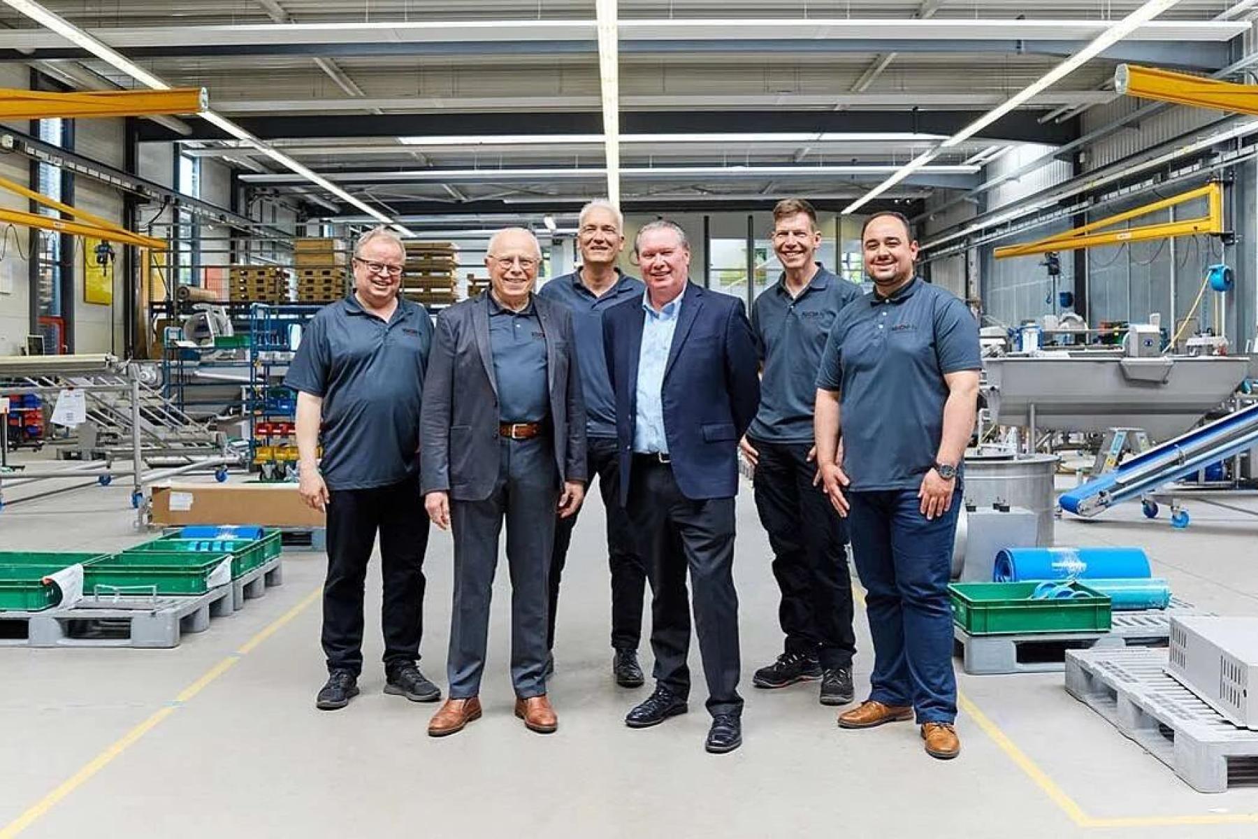 Johannes Günther, Rudolf Hans Zillgith, Stephan Zillgith, Eric Lefebvre stehen in einer Fabrikhalle mit Maschinen und Förderbändern