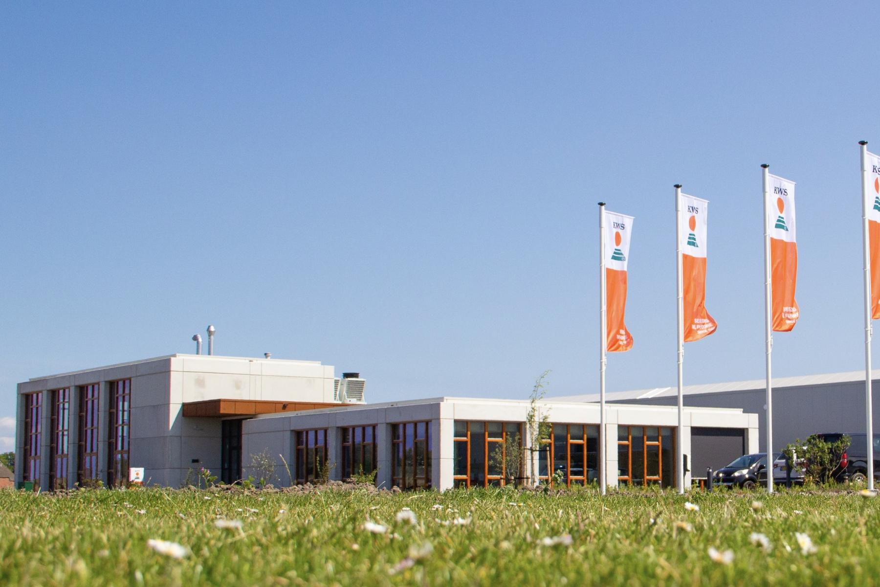 Forschungs- und Entwicklungszentrum mit Flachbau und vier Fahnen mit Firmenlogo auf grünem Rasen