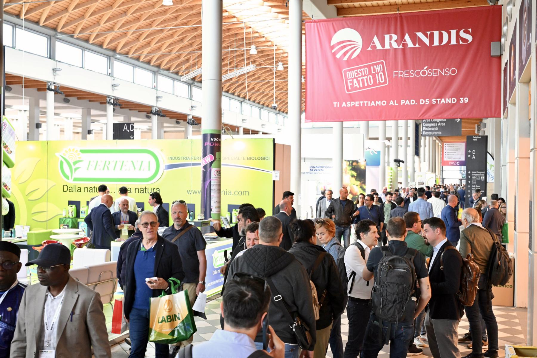 Messehalle mit zahlreichen Besuchern, Ständen von Unternehmen wie Arandis und Ferteva, Informationsbanner und helle, offene Architektur mit Holzdach.
