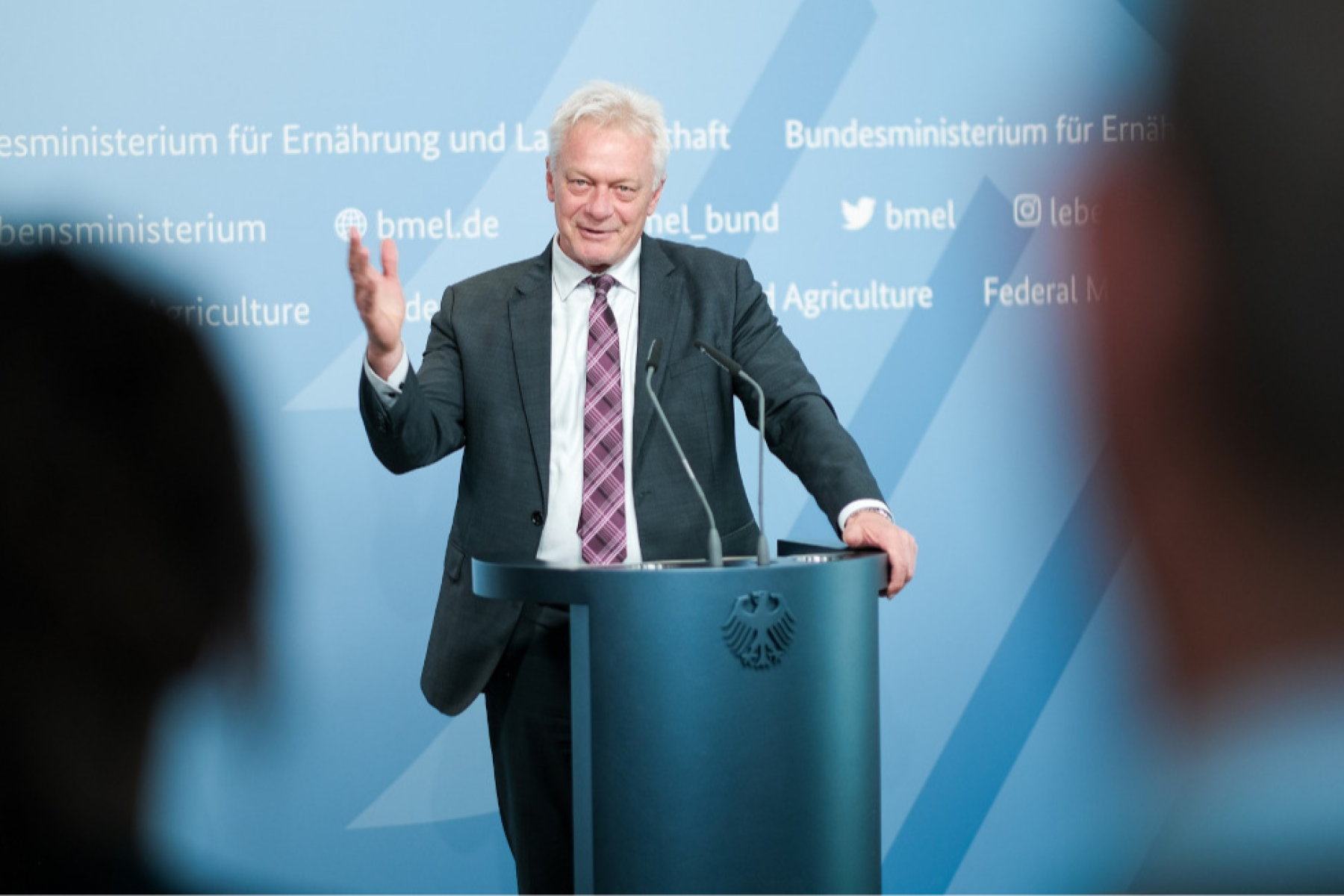 Alois Rainer steht hinter einem Rednerpult mit Bundesadler, gestikuliert mit der rechten Hand
