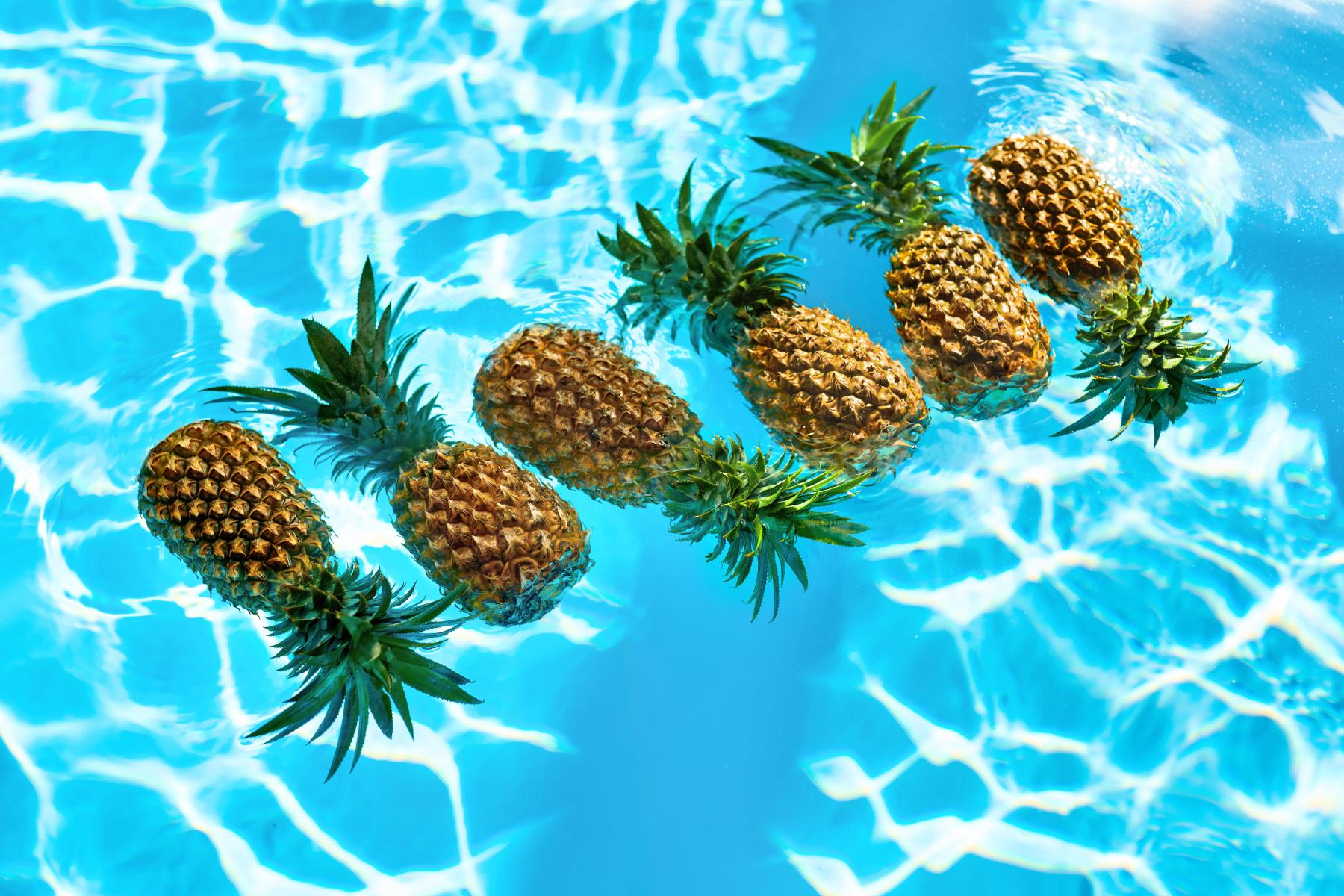 Sechs Ananas schwimmen auf der Wasseroberfläche eines Pools mit blau reflektierendem Wasser