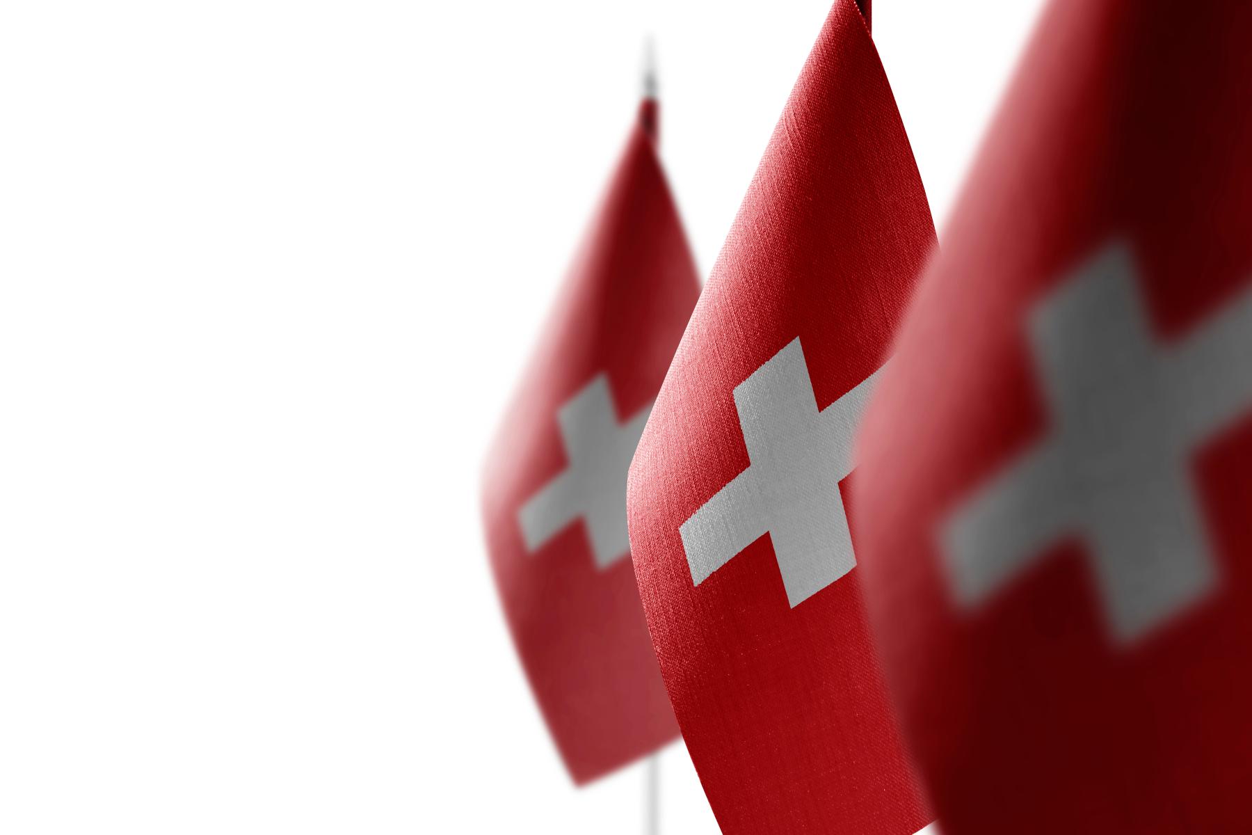 Drei Schweizer Flaggen mit weißem Kreuz auf rotem Hintergrund, unscharf im Hintergrund