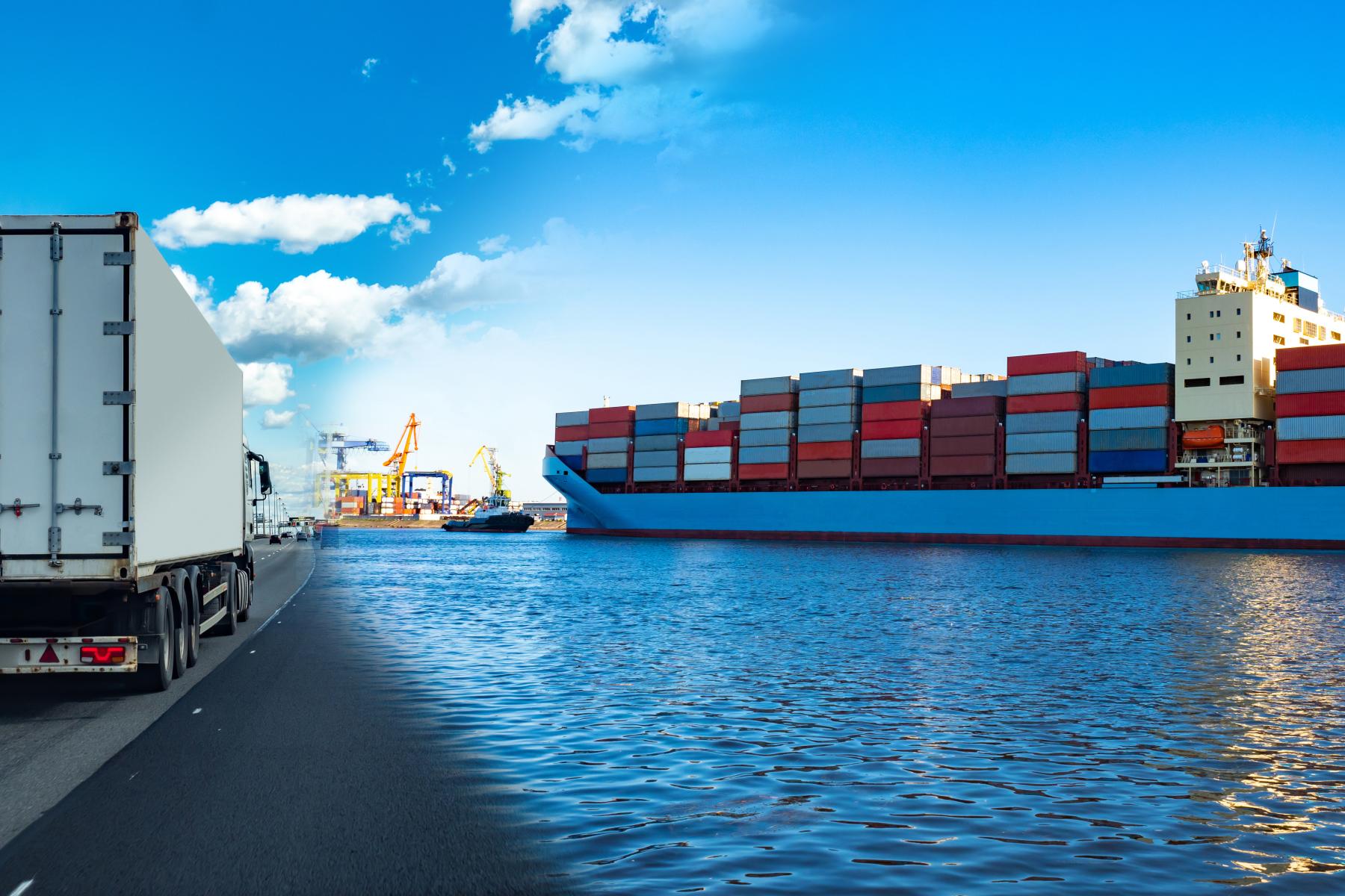 Lastwagen mit weißem Anhänger auf Straße neben Hafen mit großem Containerschiff und Kränen