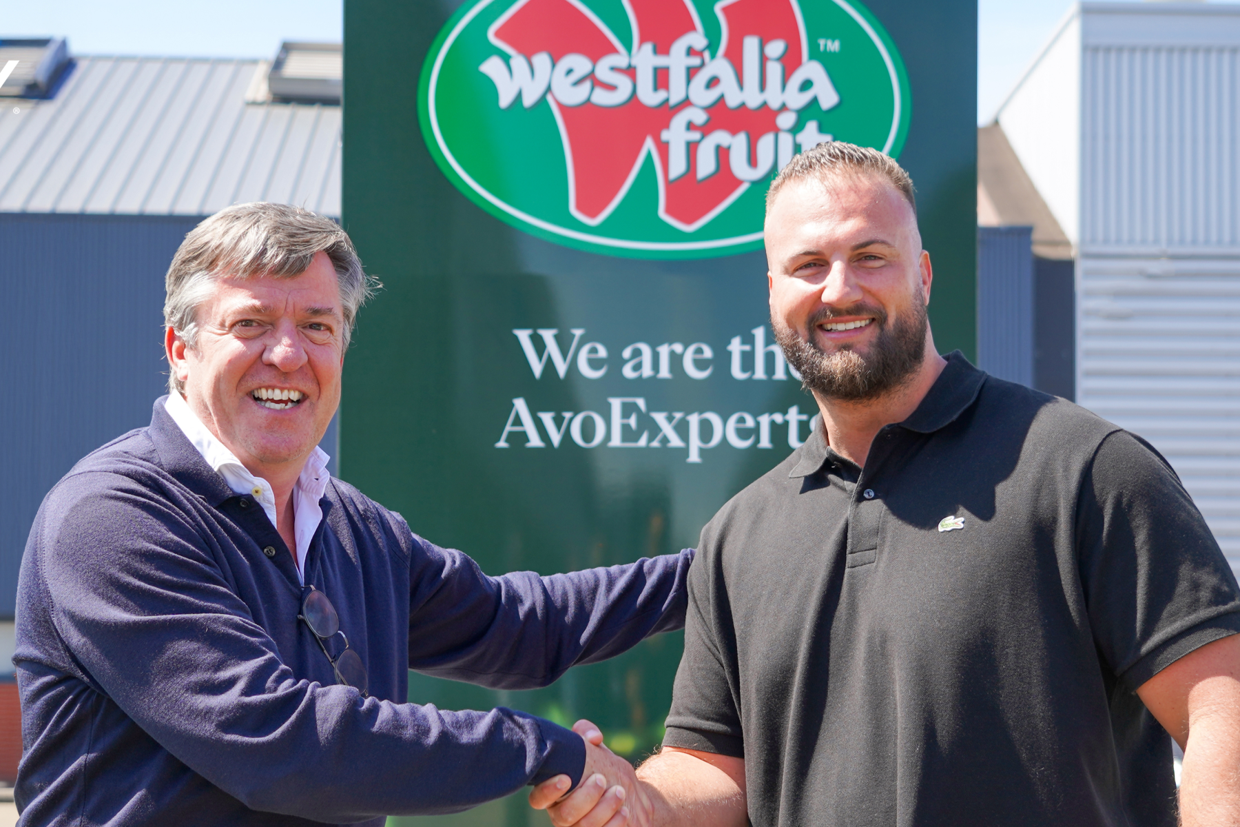 Wim Destoop und Carel van Krimpen schütteln sich vor einem Schild mit dem Logo von Westfalia Fruit die Hand