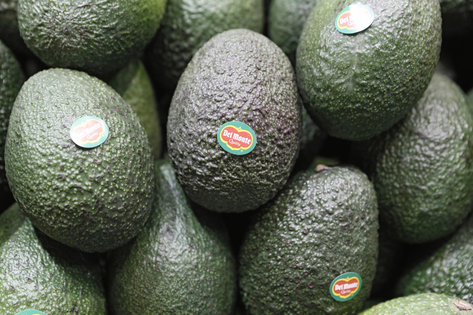 Mehrere grüne Avocados mit Del Monte Aufklebern, eng aneinander liegend