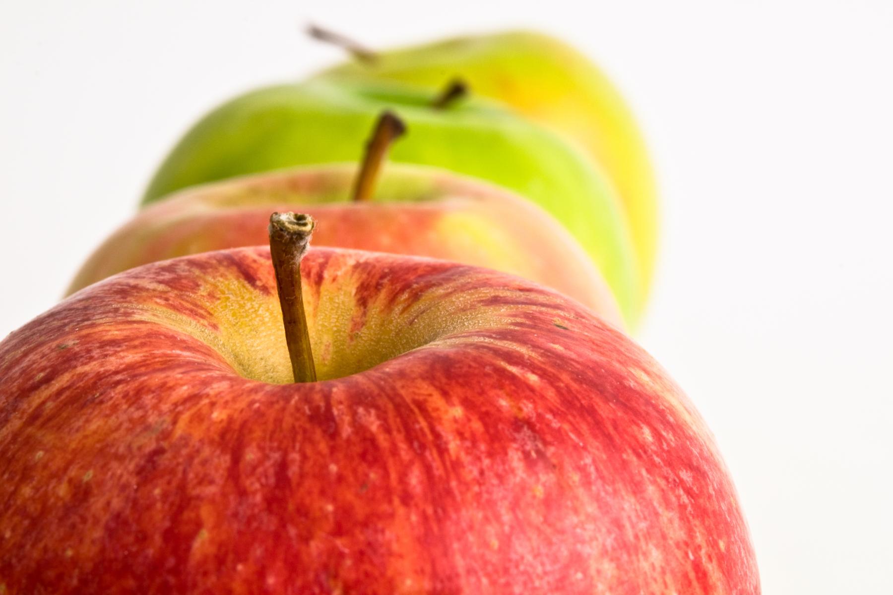 Eine Reihe von Äpfeln in verschiedenen Farben: vorne zwi rote Äpfel, gefolgt von einem grünen und einem gelben