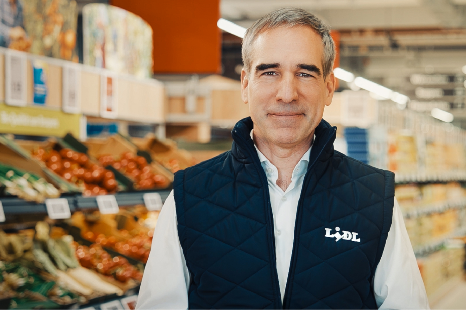 Friedrich Fuchs, Lidl-Deutschlandchef steht in einem Supermarkt mit Obst- und Gemüseregalen im Hintergrund.