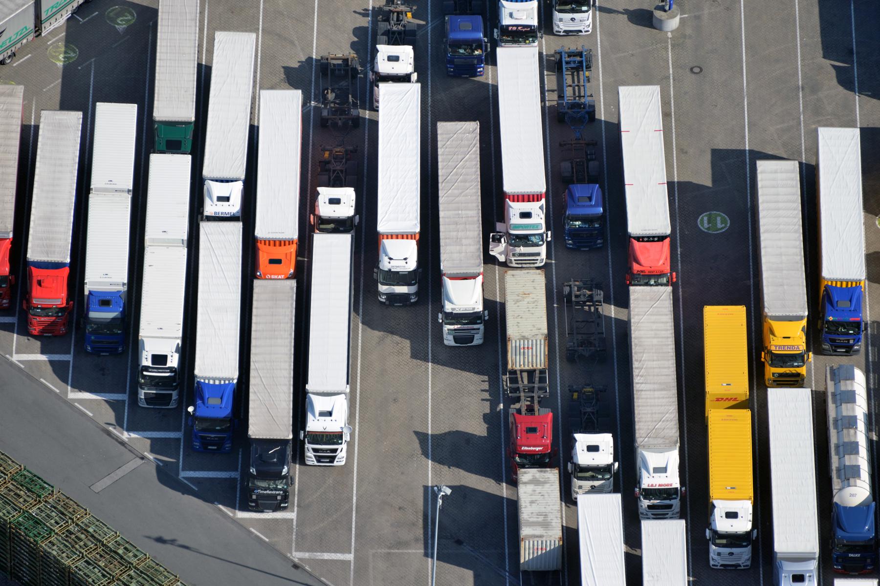 Luftaufnahme eines Parkplatzes mit mehreren Lkw in Reihen. Die Lkw haben unterschiedliche Farben, darunter rot, blau, gelb und weiß.