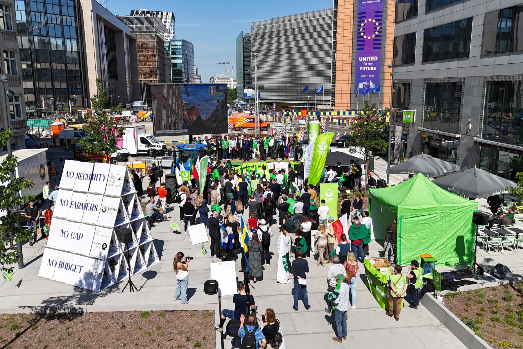 Eine Menschenmenge versammelt sich auf einem Platz mit grünen und weißen Bannern. Im Hintergrund ist ein großer Bildschirm zu sehen. Mehrere Stände und Zelte sind aufgestellt.