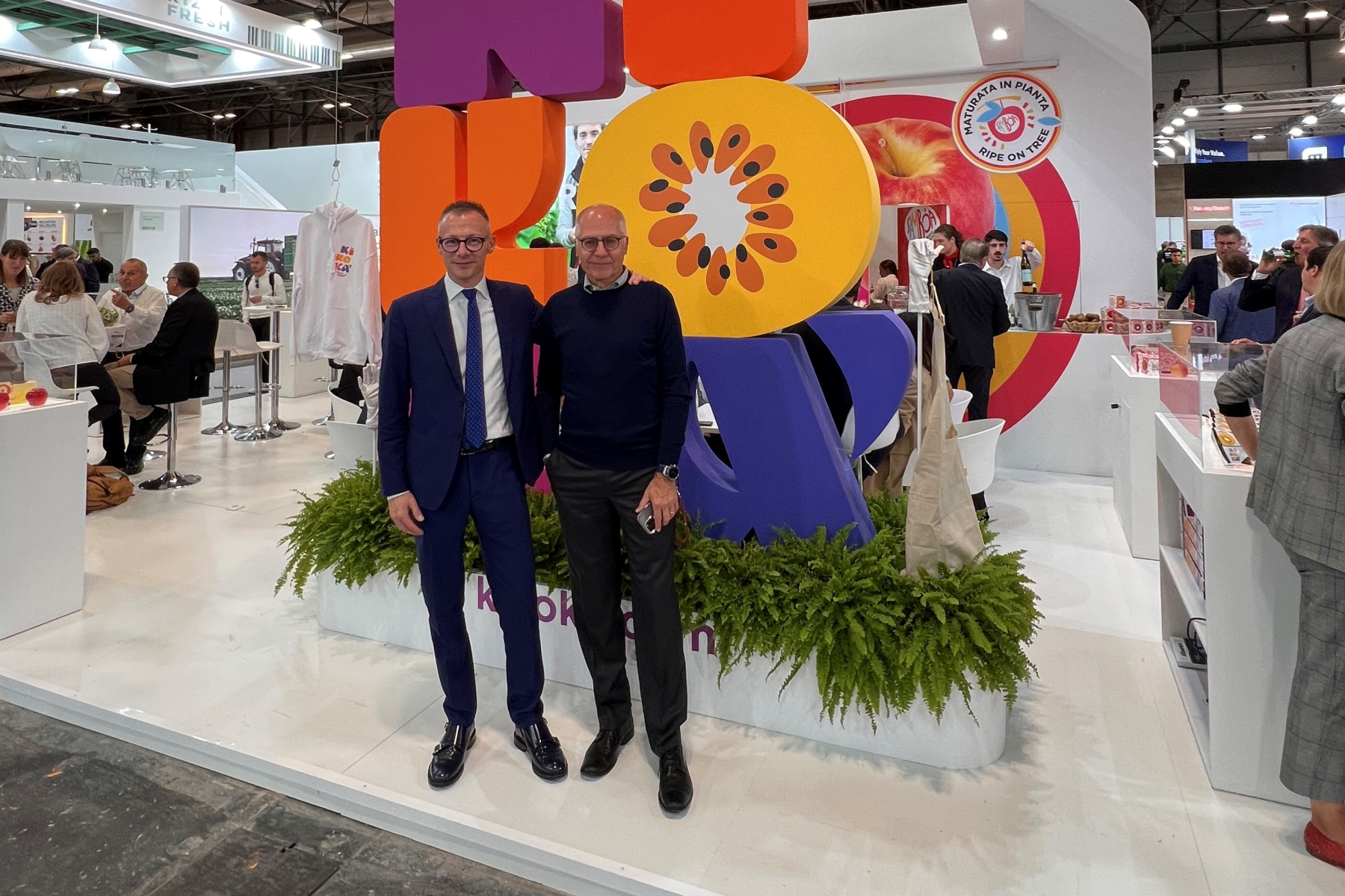 Fabio Zanesco links und Gerhard Dichgans stehen nebeneinander vor einem Messestand mit bunten, großen Buchstaben, die 'Kikokà' bilden