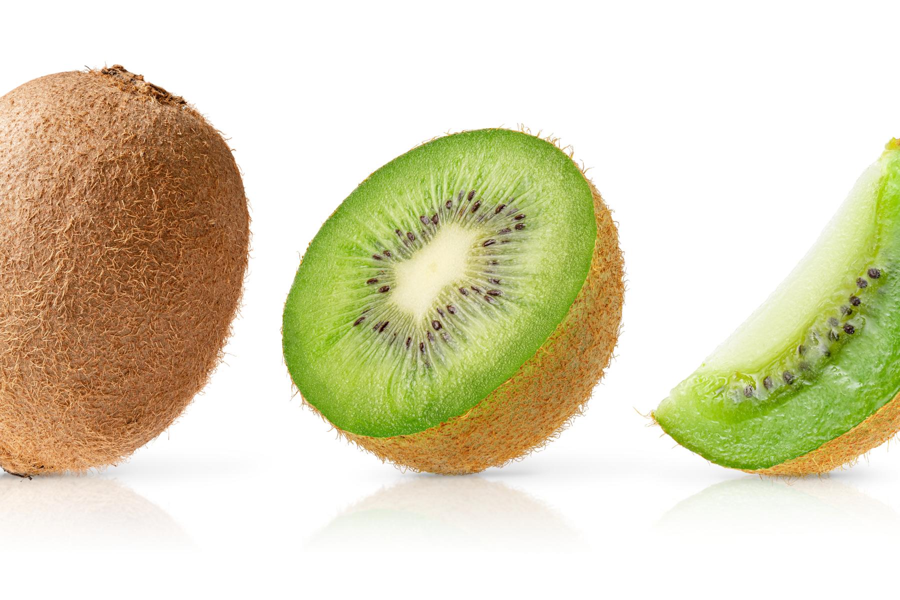 Eine ganze Kiwi links, in der Mitte eine halbierte Kiwi mit grünem Fruchtfleisch und schwarzen Kernen, rechts ein Viertel einer Kiwi mit grünem Fruchtfleisch.