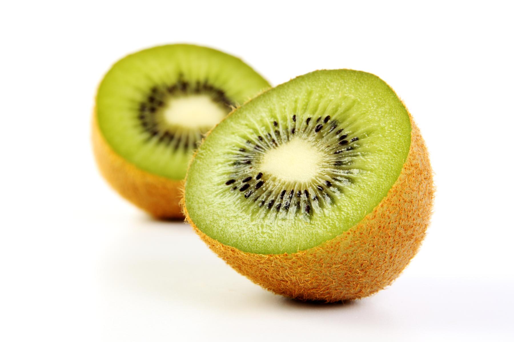 Zwei Hälften einer Kiwi mit grünem Fruchtfleisch und schwarzen Kernen, die auf einer weißen Fläche liegen.