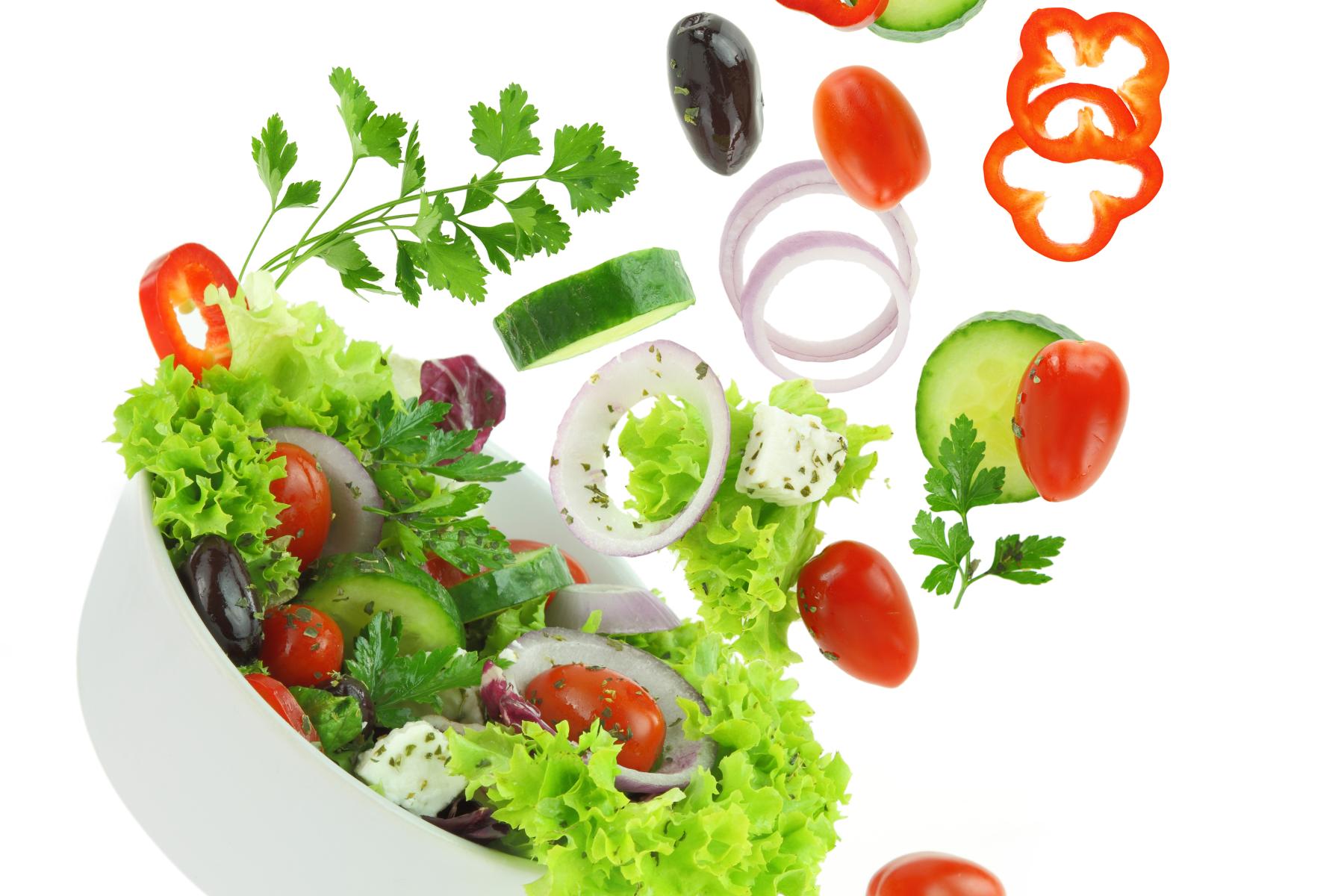 Eine weiße Schüssel mit gemischtem Salat, darunter grüne Blätter, Kirschtomaten, Gurkenscheiben, rote Paprika und Zwiebelringe, die in der Luft schweben.