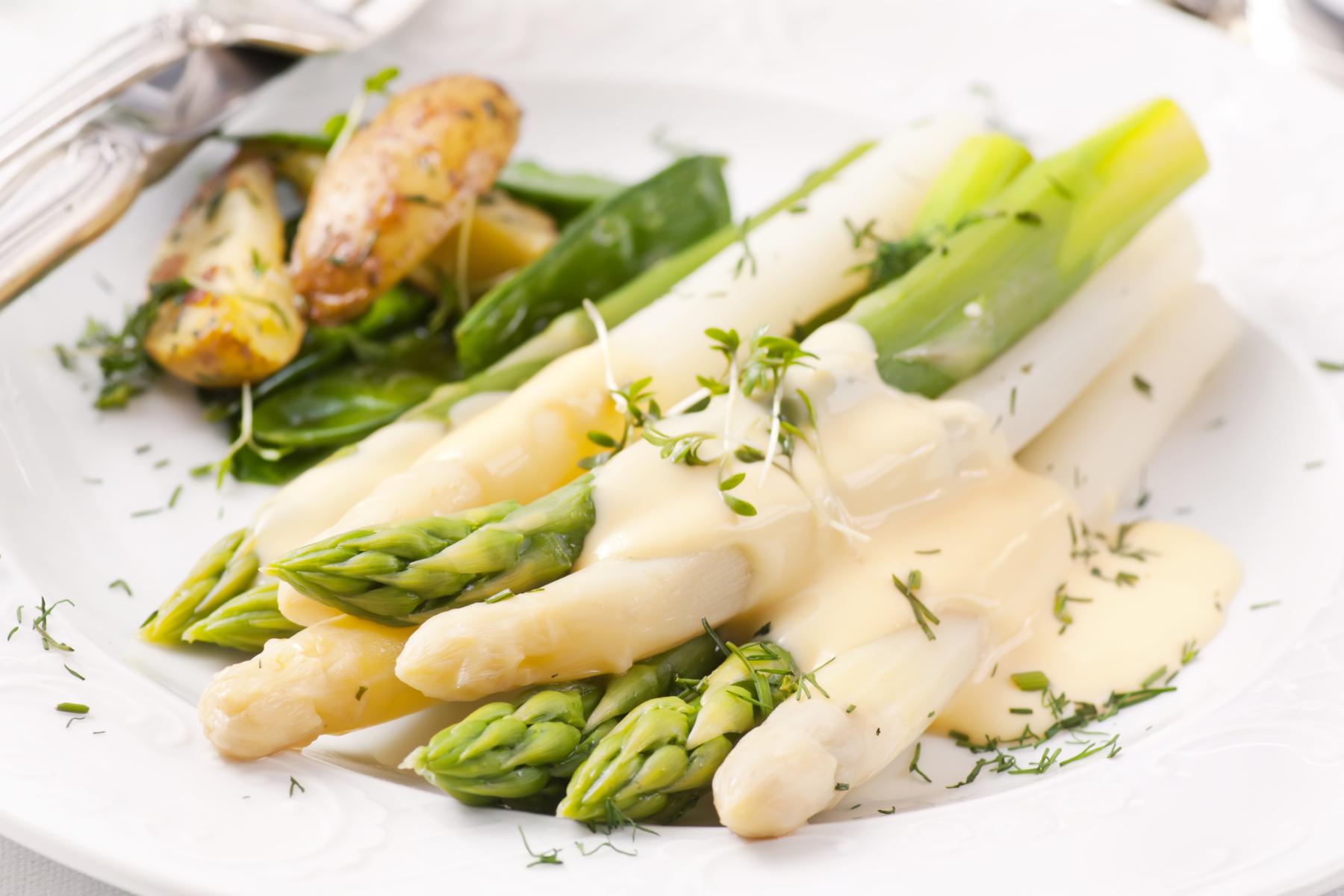 Ein Teller mit Spargel, grünem Gemüse und kleinen Kartoffeln. Der Spargel ist mit einer hellen Sauce und frischen Kräutern garniert.