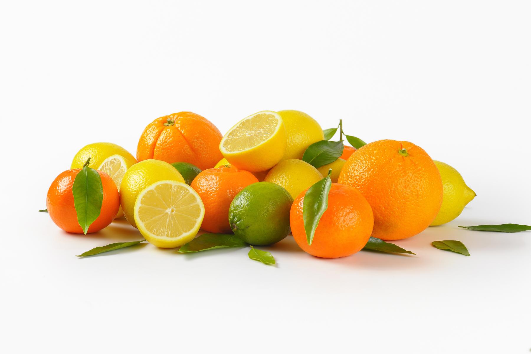 Eine Anordnung von Orangen, Zitronen und einer Limette mit grünen Blättern, einige Früchte sind halbiert und zeigen das Fruchtfleisch.