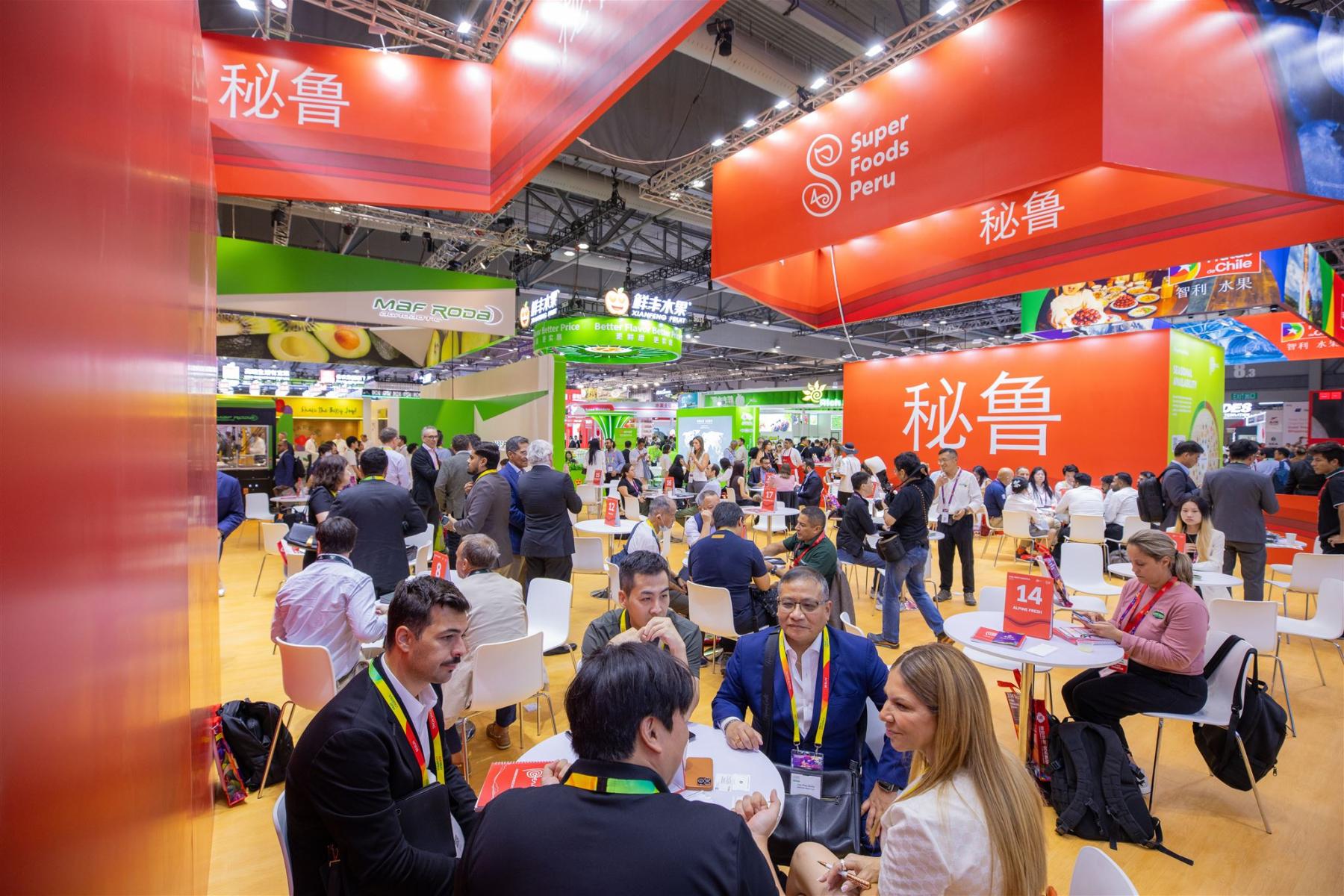 Messehalle mit vielen Personen an Tischen, rotes Banner mit 'Super Foods Peru' und chinesischen Schriftzeichen, lebhafte Atmosphäre.