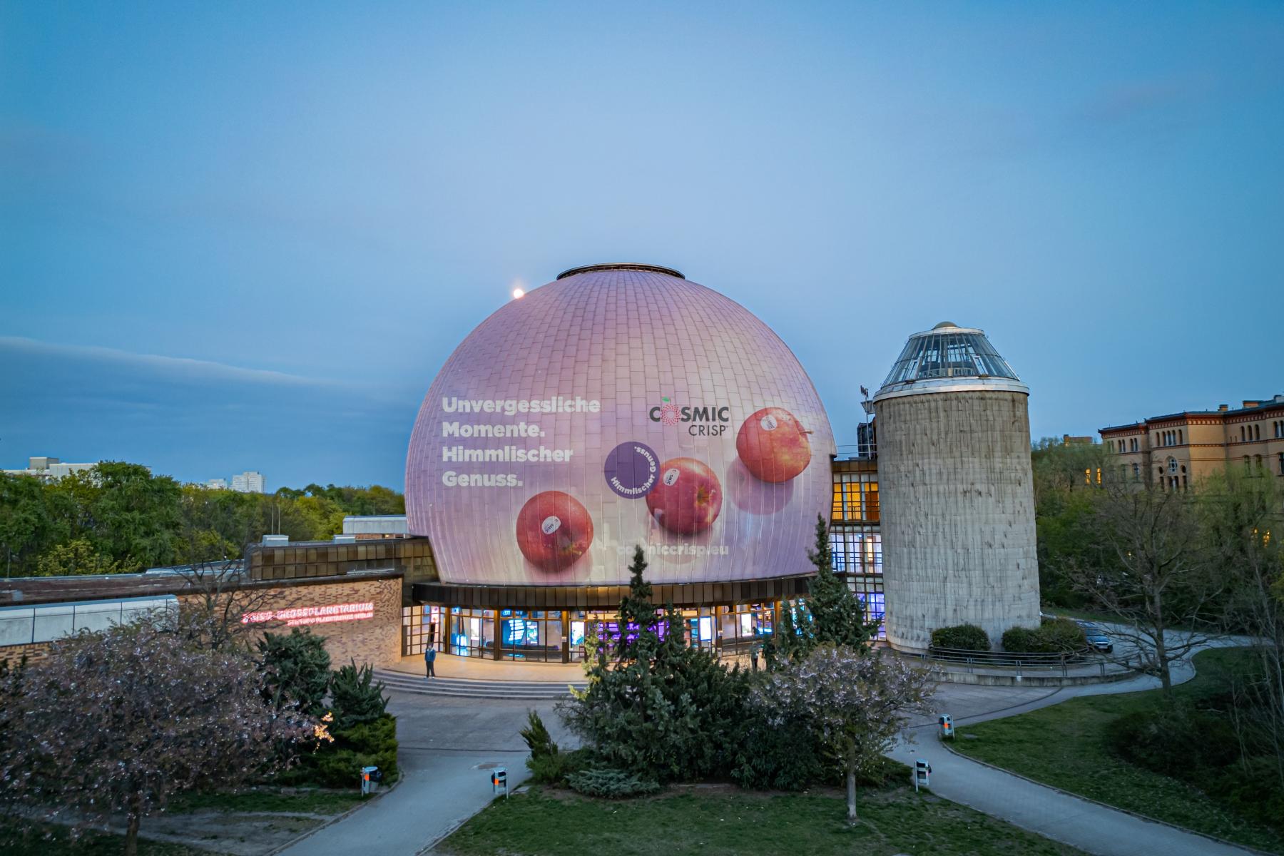 Das Berliner Planetarium mit einer großen Projektion von Cosmic Crisp® Äpfeln auf der Kuppel. Text: 'Unvergessliche Momente. Himmlischer Genuss.'