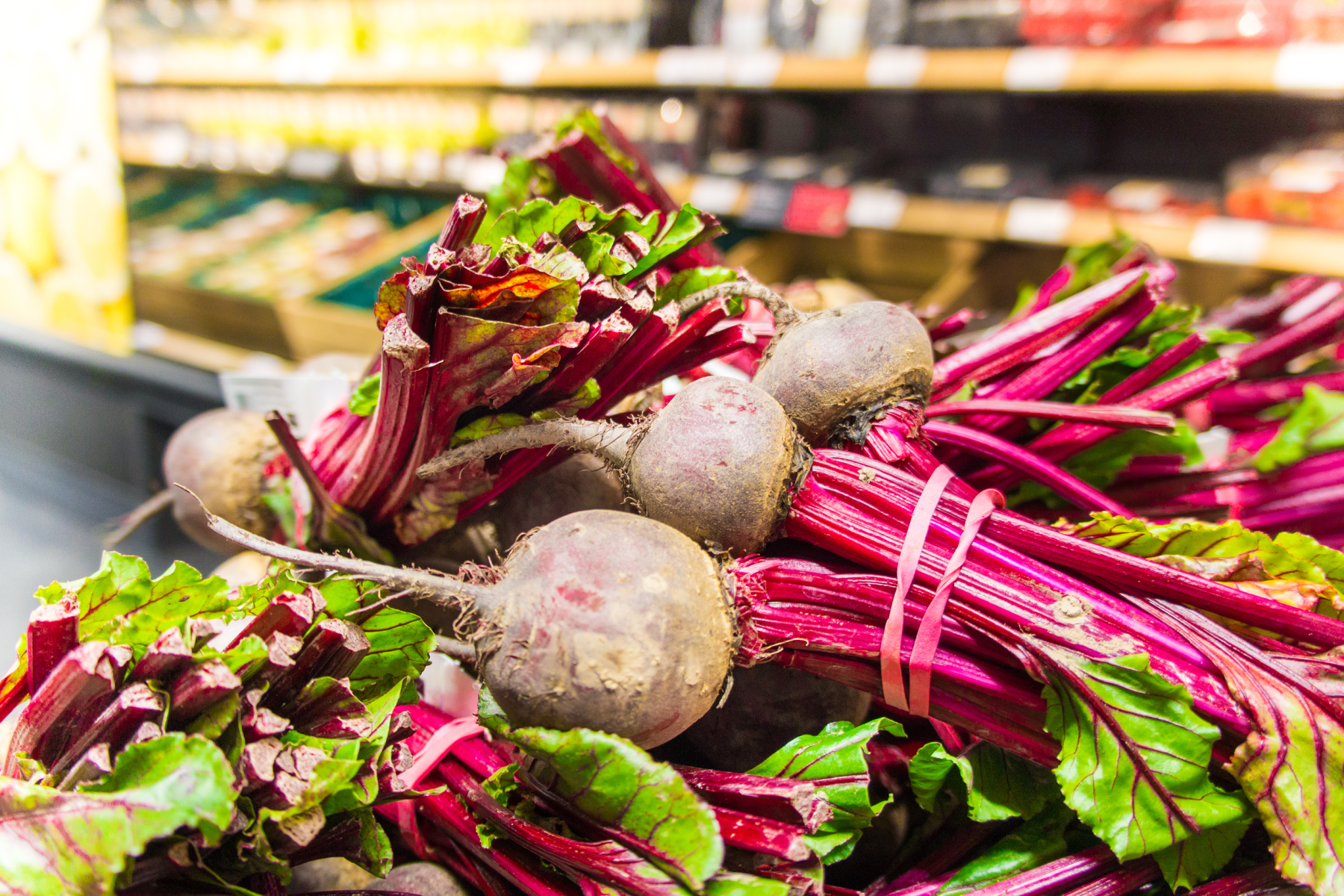 Bund frischer Rote Beete mit grünen Blättern, violetten Stielen und erdigen Knollen, in einem Supermarktregal.