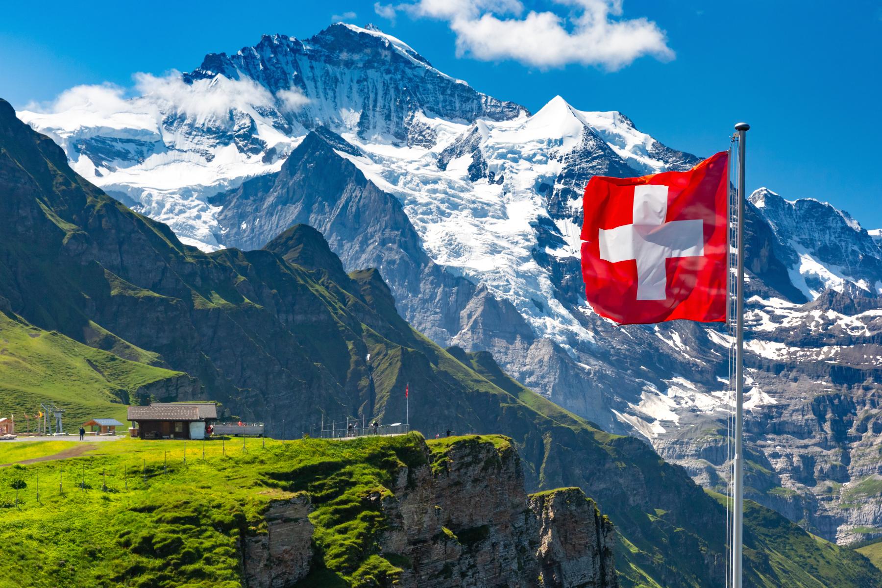 Schweizer Fahne weht vor einem schneebedeckten Berg und einer Hütte