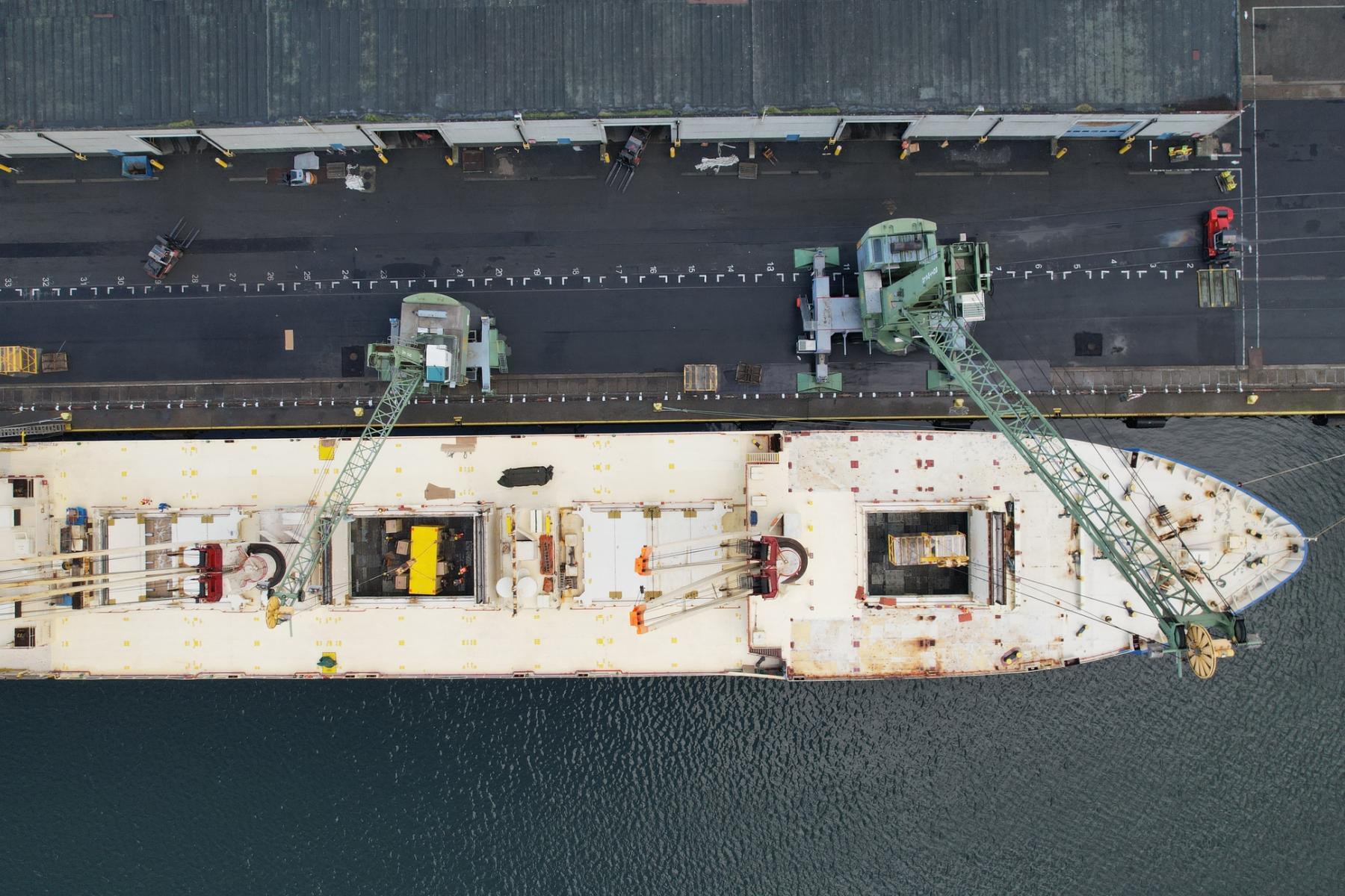 Luftaufnahme eines beladenen Frachtschiffs am Hafen mit Kränen und Lagerbereich am Kai