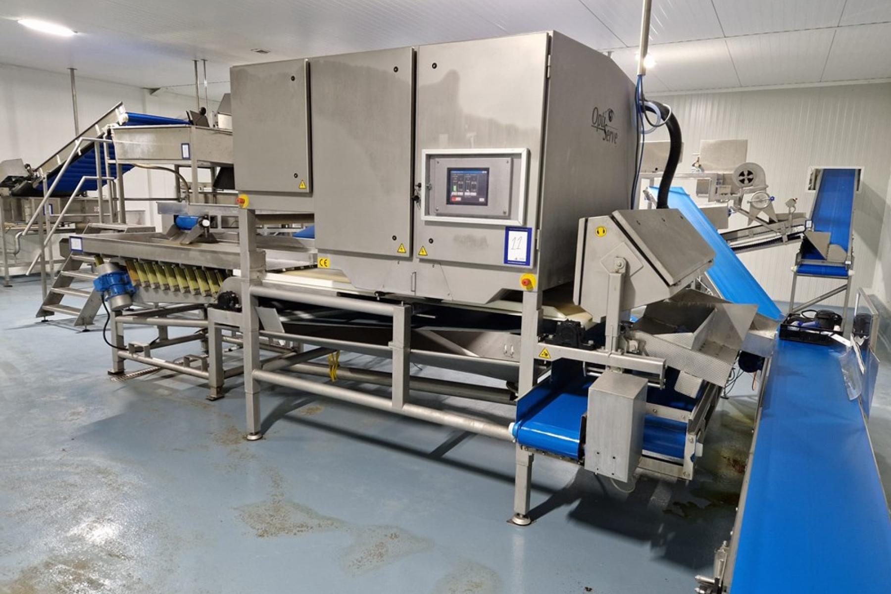 Große industrielle Maschine mit mehreren Förderbändern und Steuerungstafel in einer Produktionshalle mit grauem Boden.