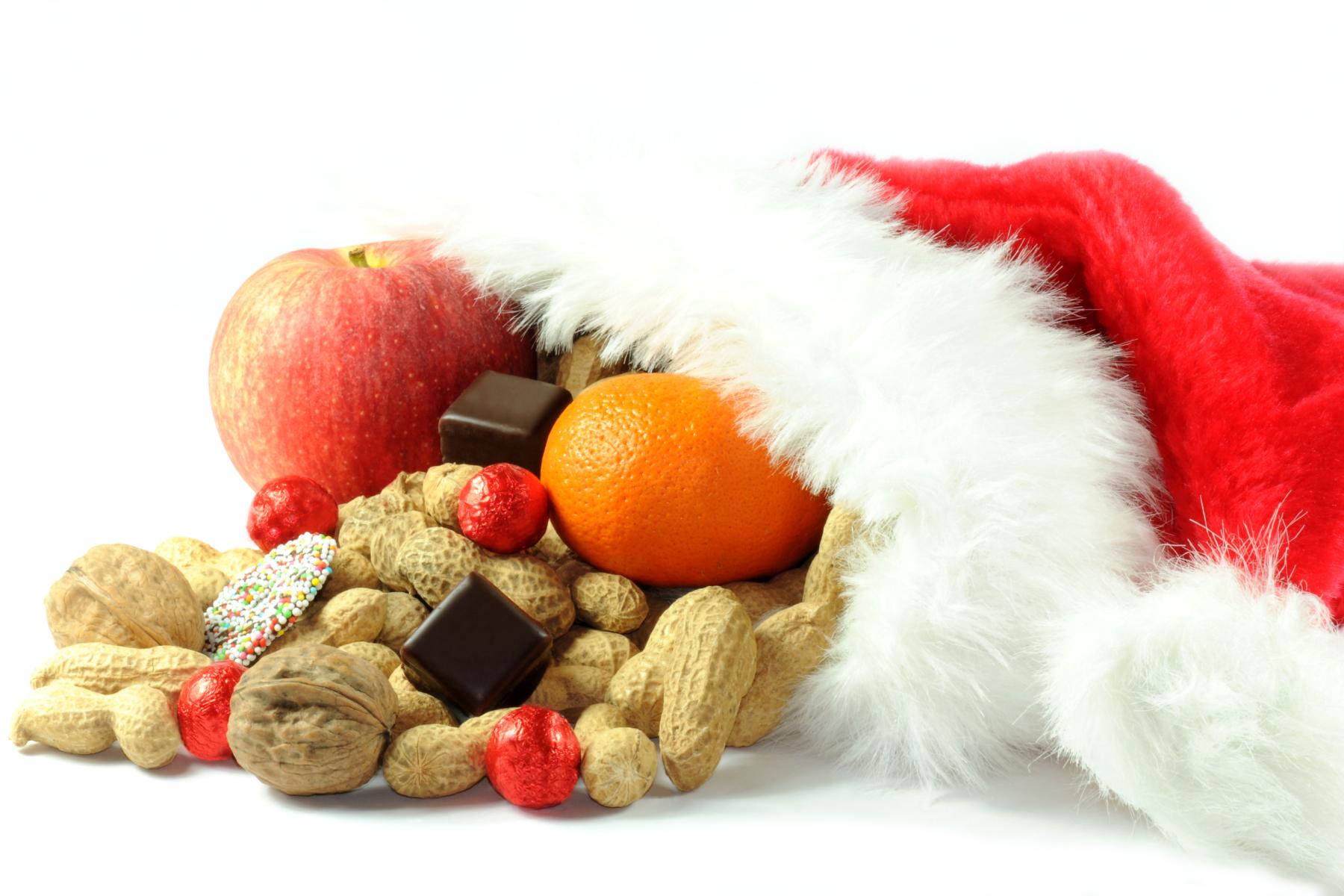 Rote Nikolausmütze, in der sich Äpfel, Citrusfrüchte, Nüsse und Süßigkeiten befinden.