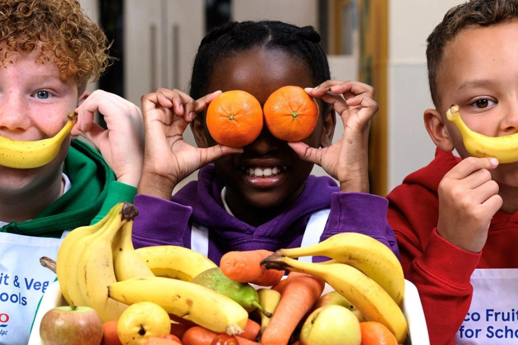 Kinder halten sich Bananen und Mandarinen vor Augen und Mund