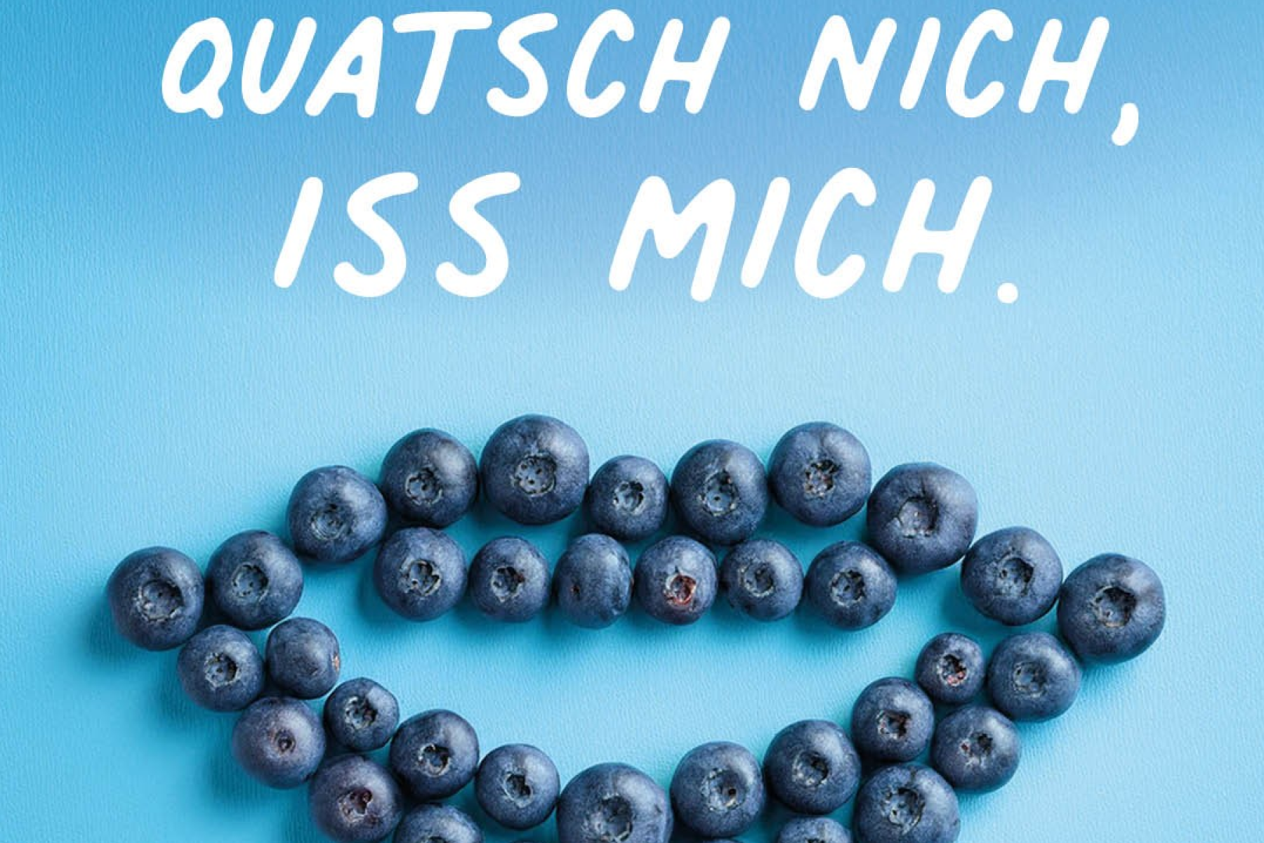 Mehrere Heidelbeeren bilden die Form eines Mundes auf blauem Hintergrund, darüber der Text 'QUATSCH NICH, ISS MICH.' in weißer Schrift.