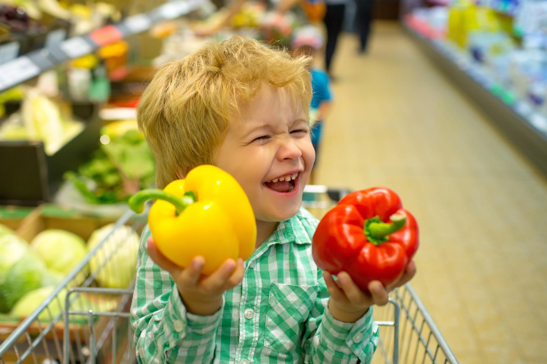 Junge lacht und hält rote und gelbe Paprika in der Hand