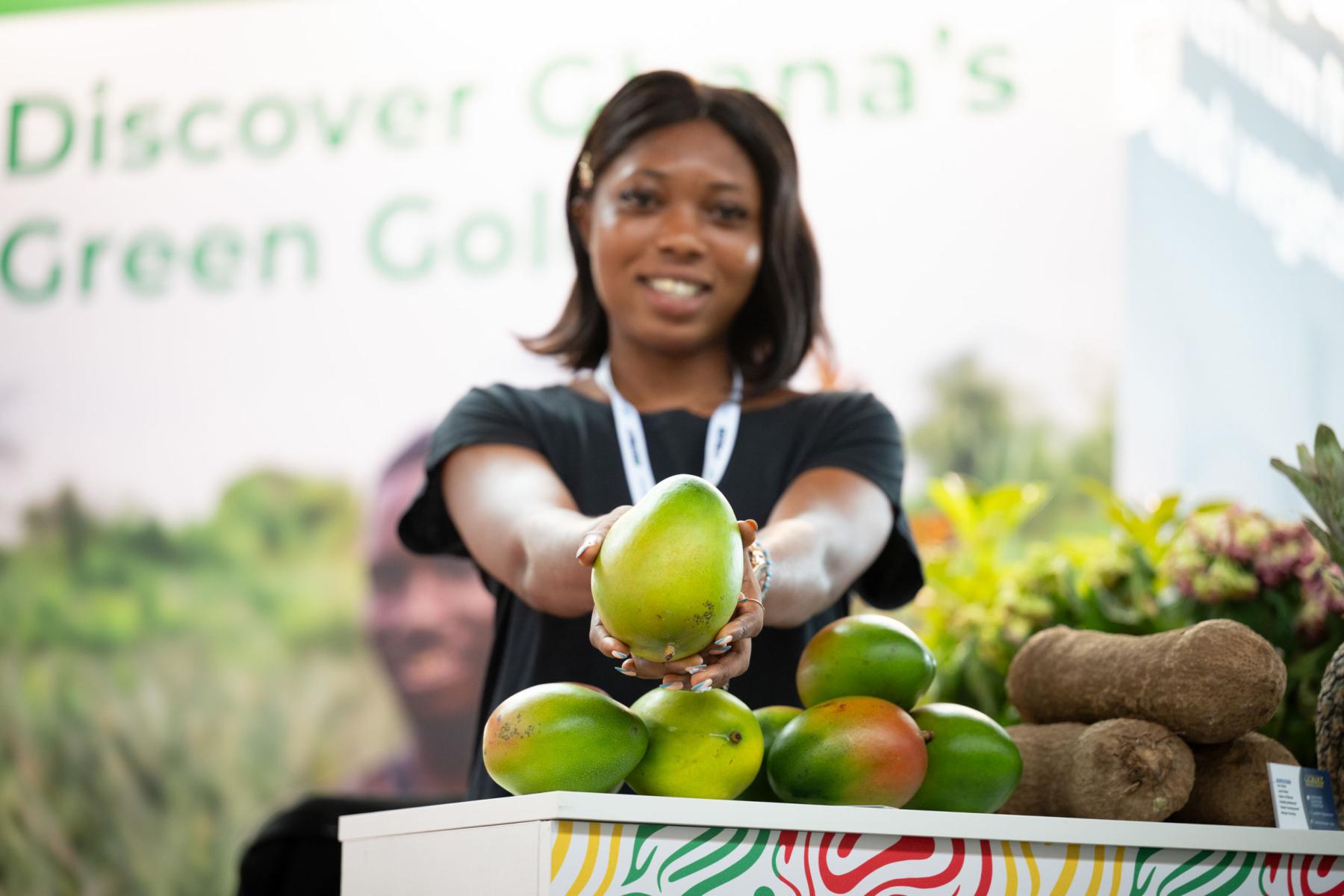 Eine Ausstellerin auf der Macfrut 2025 hält eine Mango in die Kamera